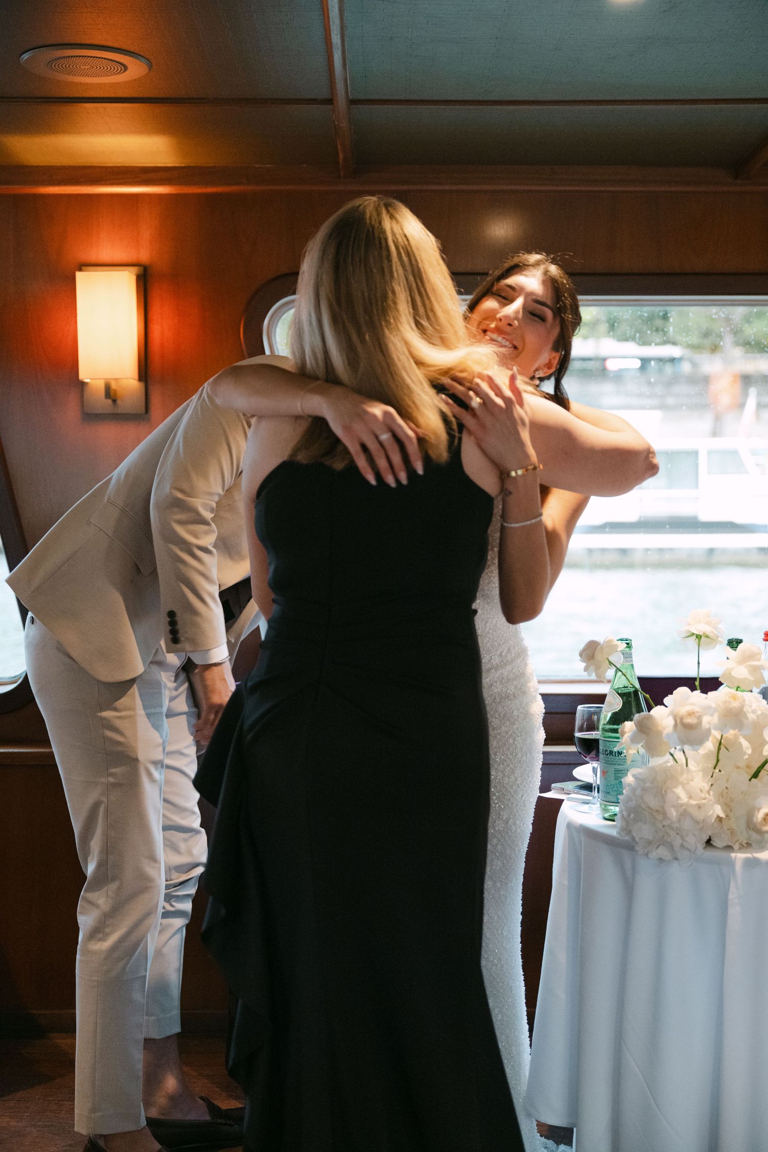 A bride in a white sequin gown embraces a guest in a warm hug at her boat wedding reception.