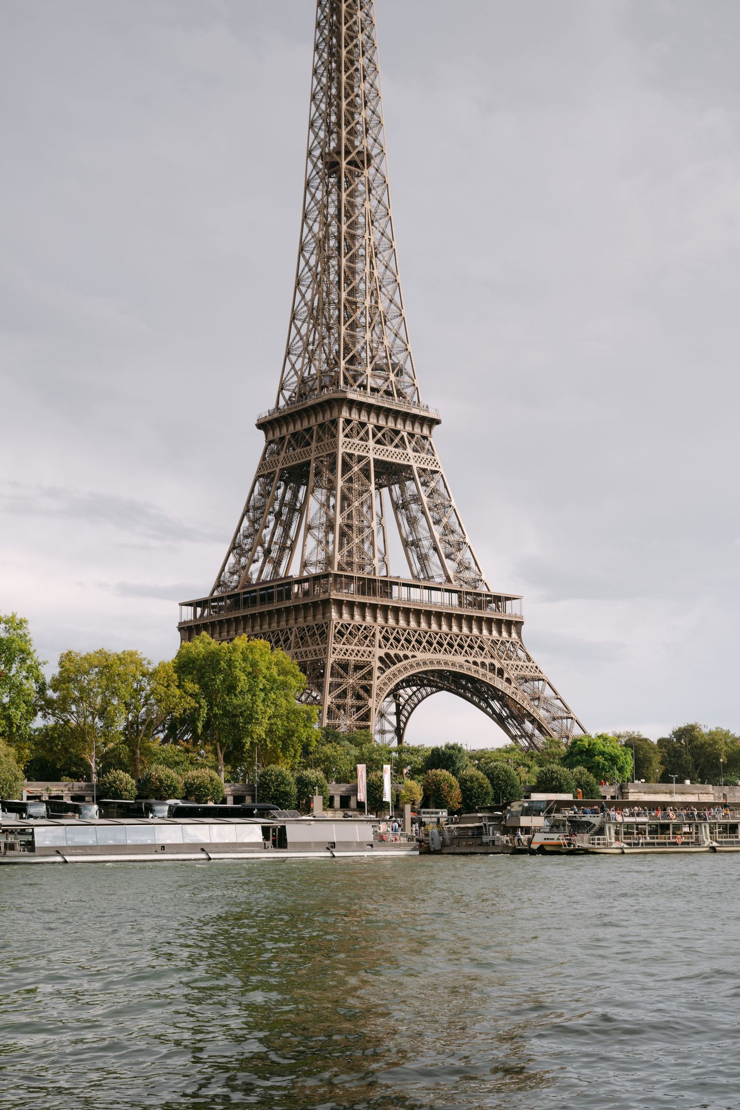 The iconic Eiffel Tower rises above the Seine River under a cloudy sky in Paris, France.