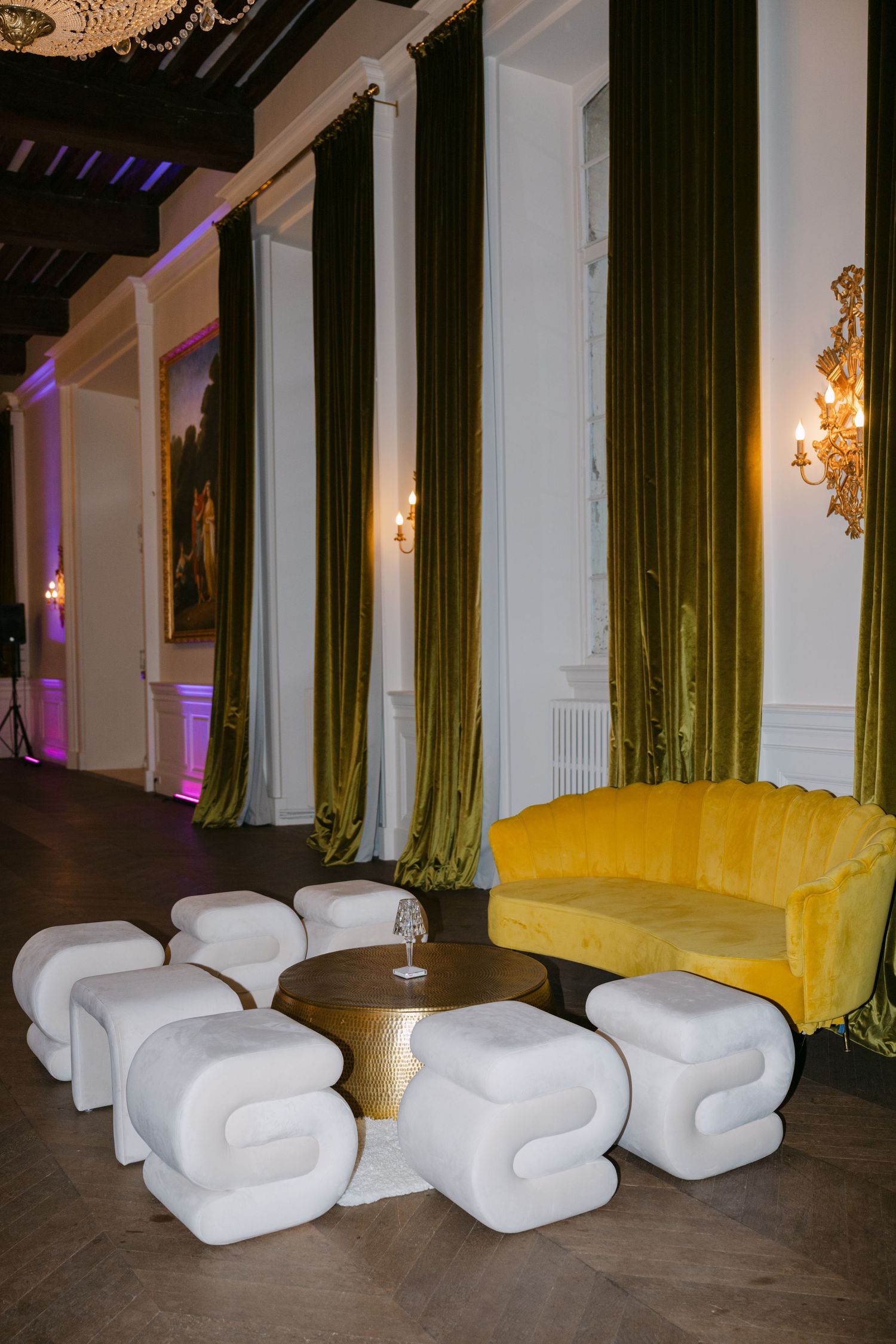 Luxurious wedding reception lounge with yellow velvet sofa, white ottomans, and olive green drapes.