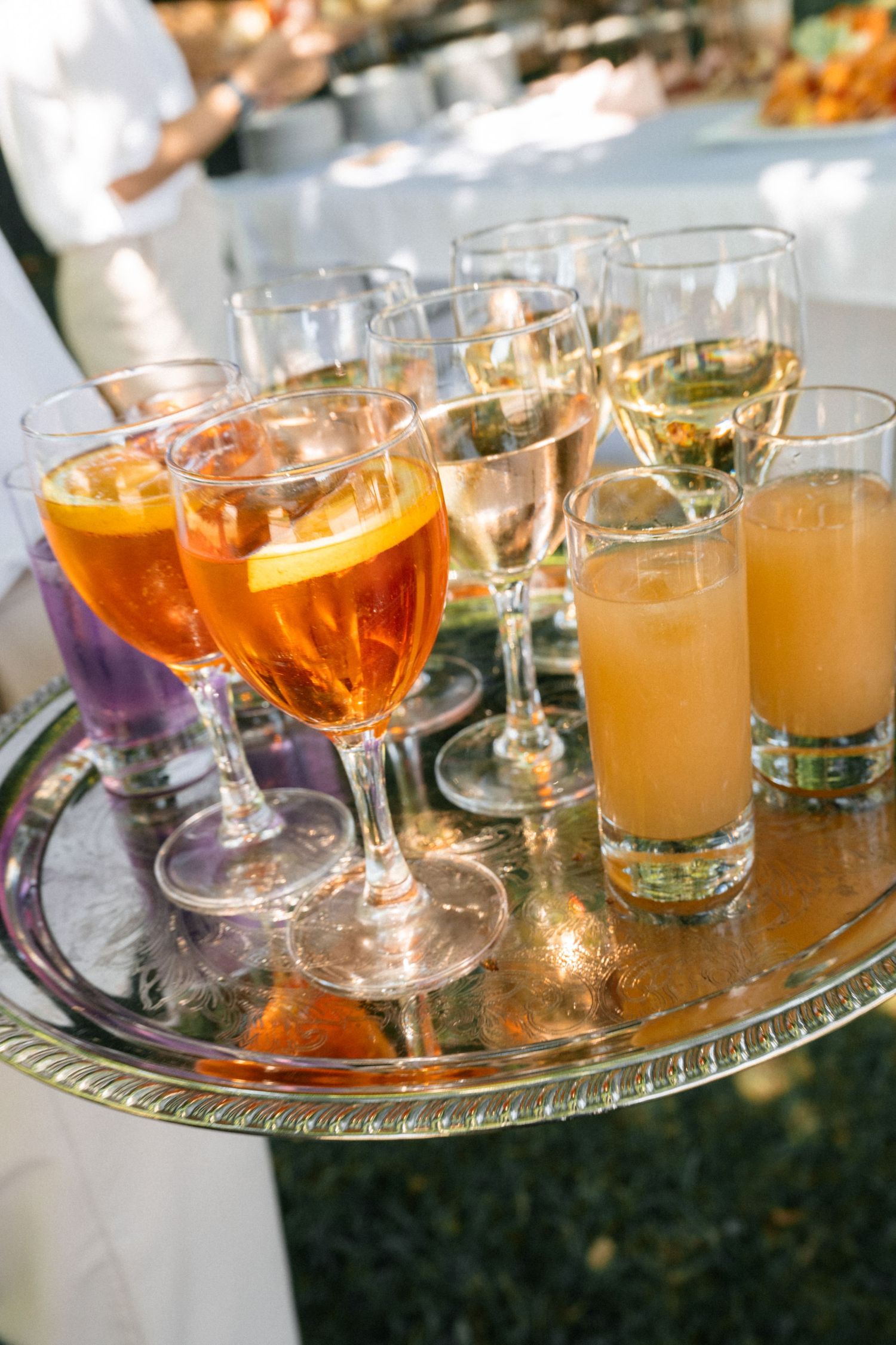 Silver tray with Aperol spritz cocktails, champagne, and orange juice glasses at an outdoor wedding reception.