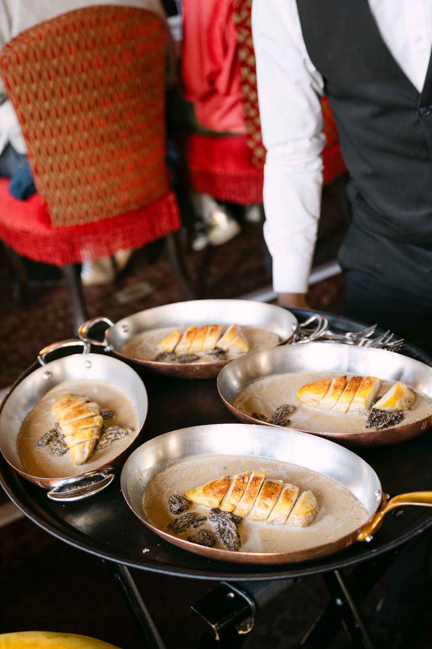 Waiter serving golden pastries in copper pans at elegant French restaurant.