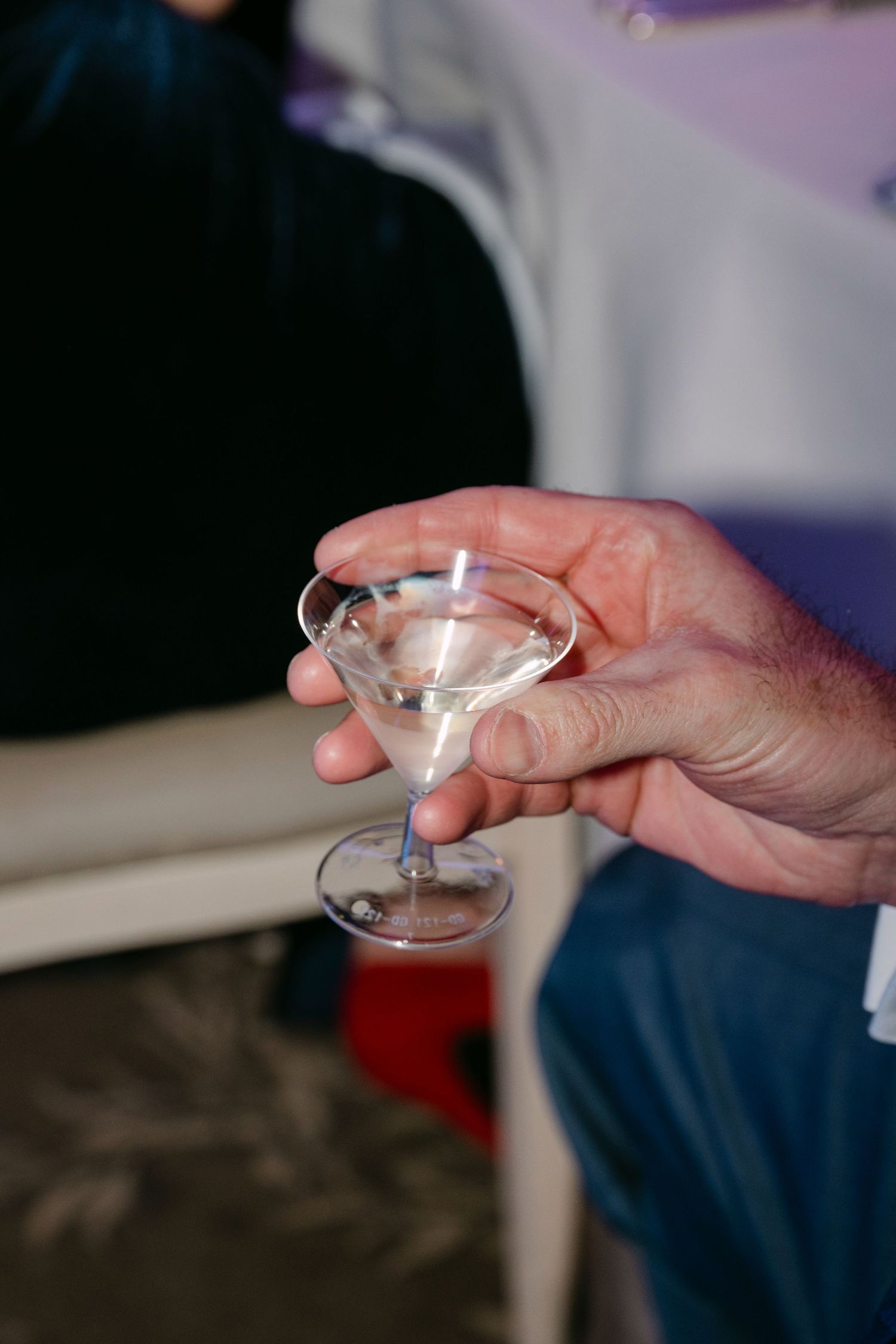 Guest holds small martini glass with clear cocktail at elegant wedding reception event.