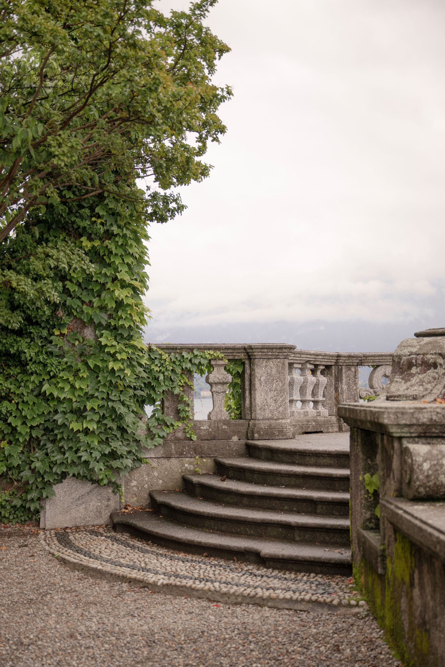 Stone balustrade staircase with ivy-covered walls in an elegant classical garden terrace on a cloudy day.