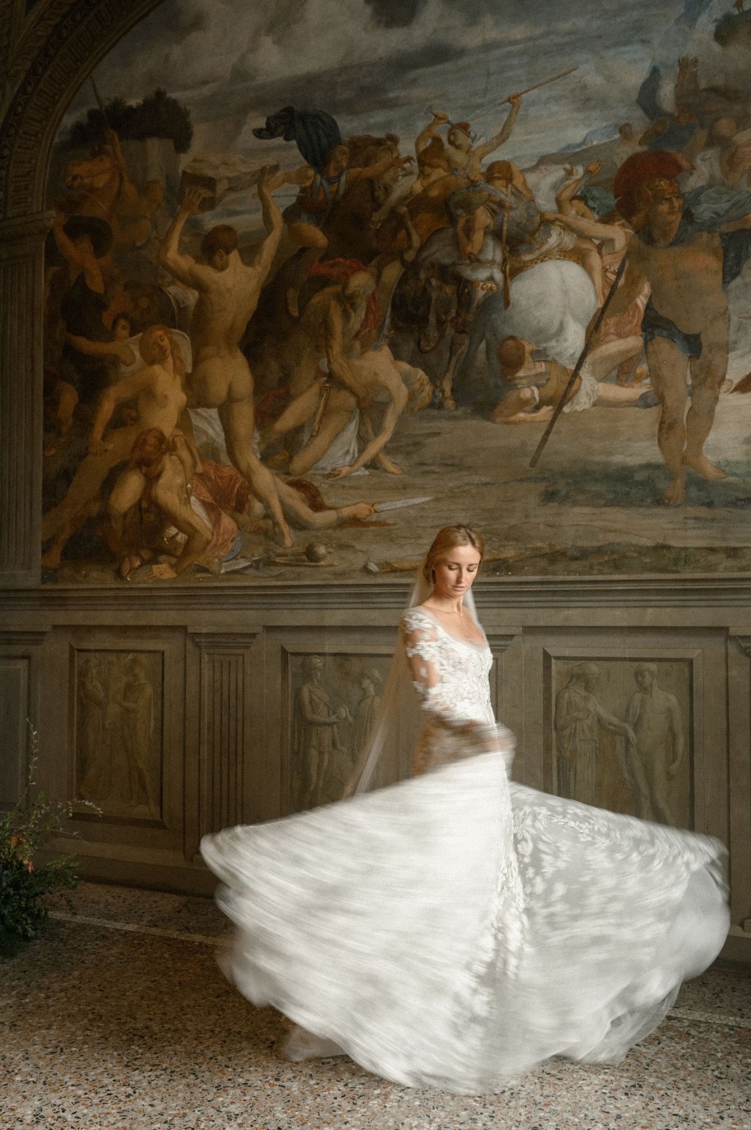 Bride in white lace gown twirling before a grand Renaissance fresco mural in an ornate Italian palazzo.