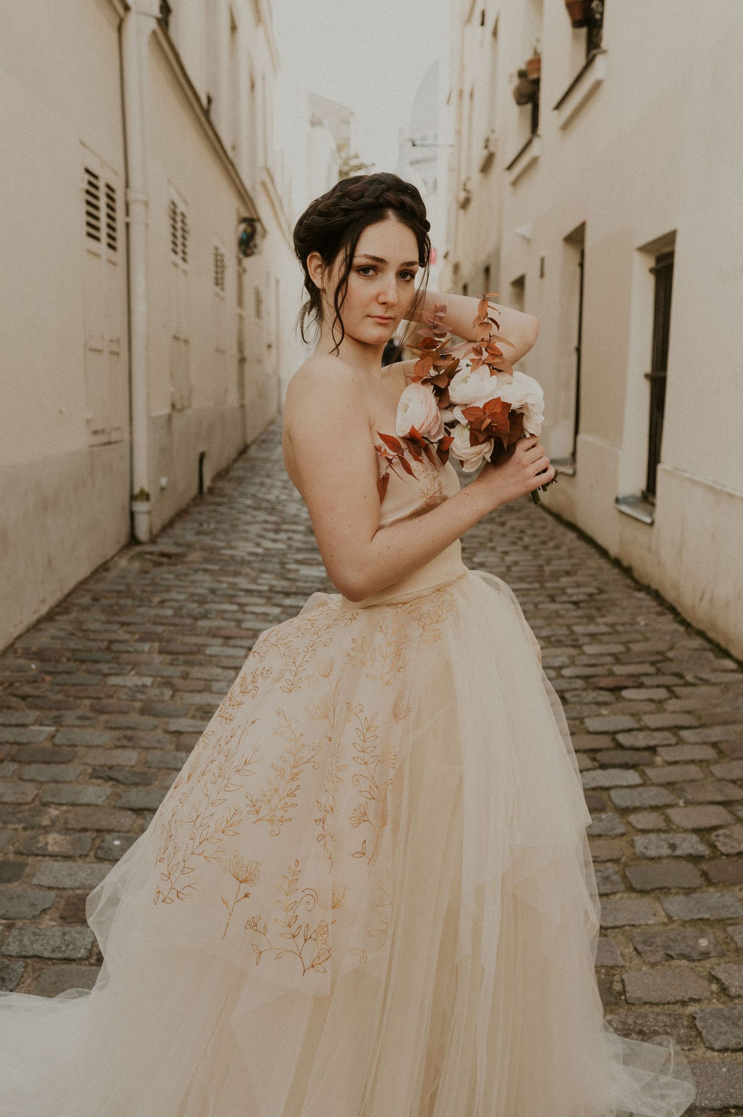 A stunning wedding dress with layers of tulle and delicate floral details captured in a cobblestone alley.