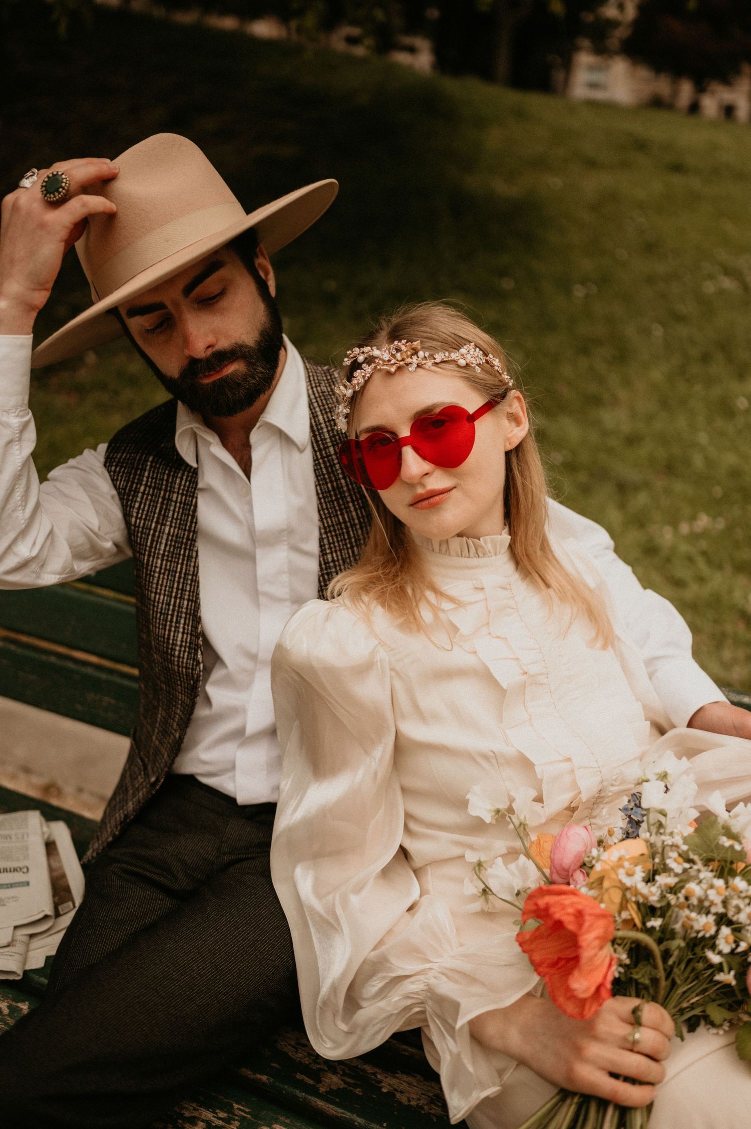 A romantic outdoor portrait featuring vintage fashion, a floral bouquet, and red heart-shaped sunglasses.