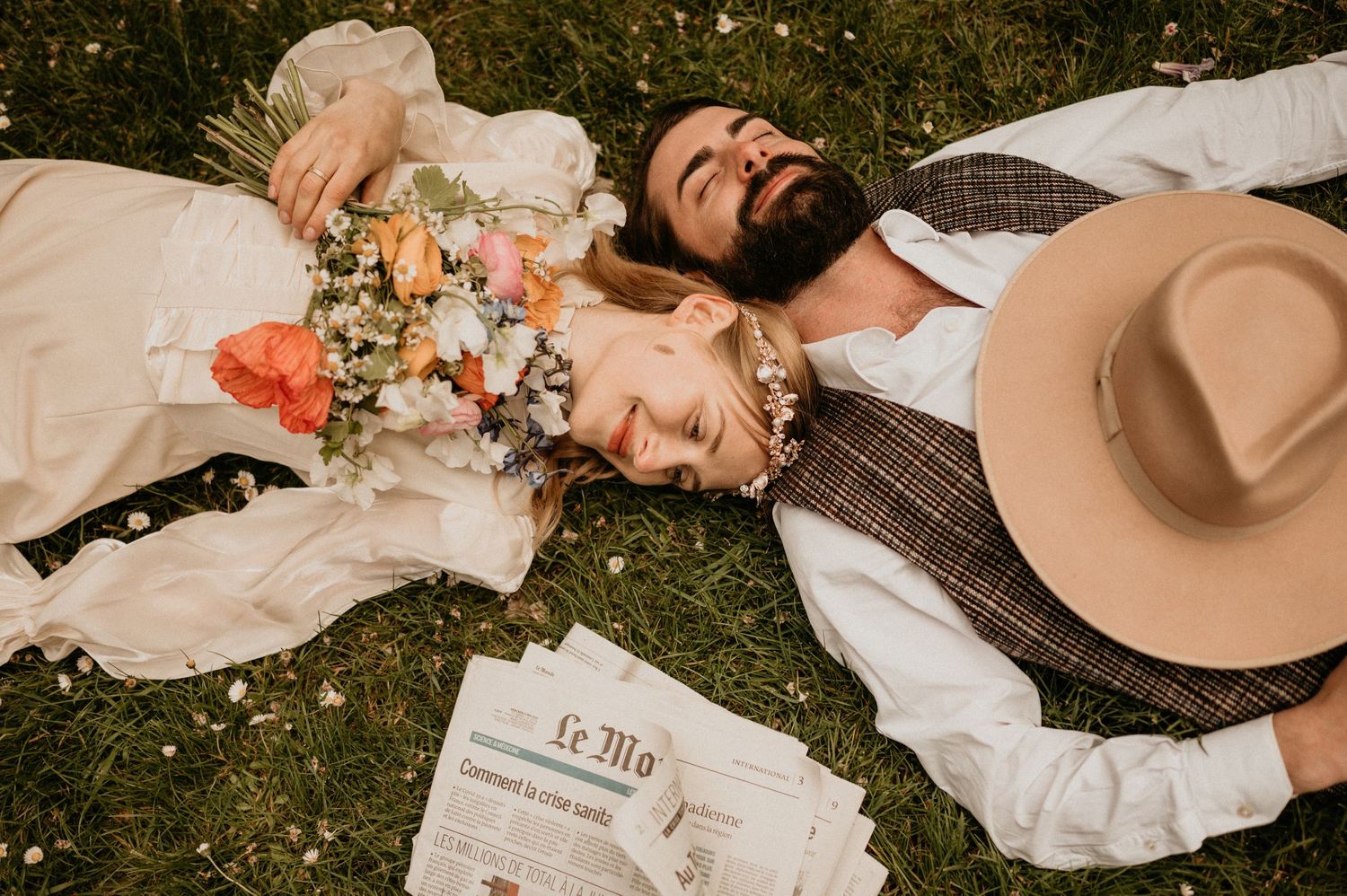 Romantic couple lying on grass with flowers and Le Monde newspaper in dreamy autumn setting.