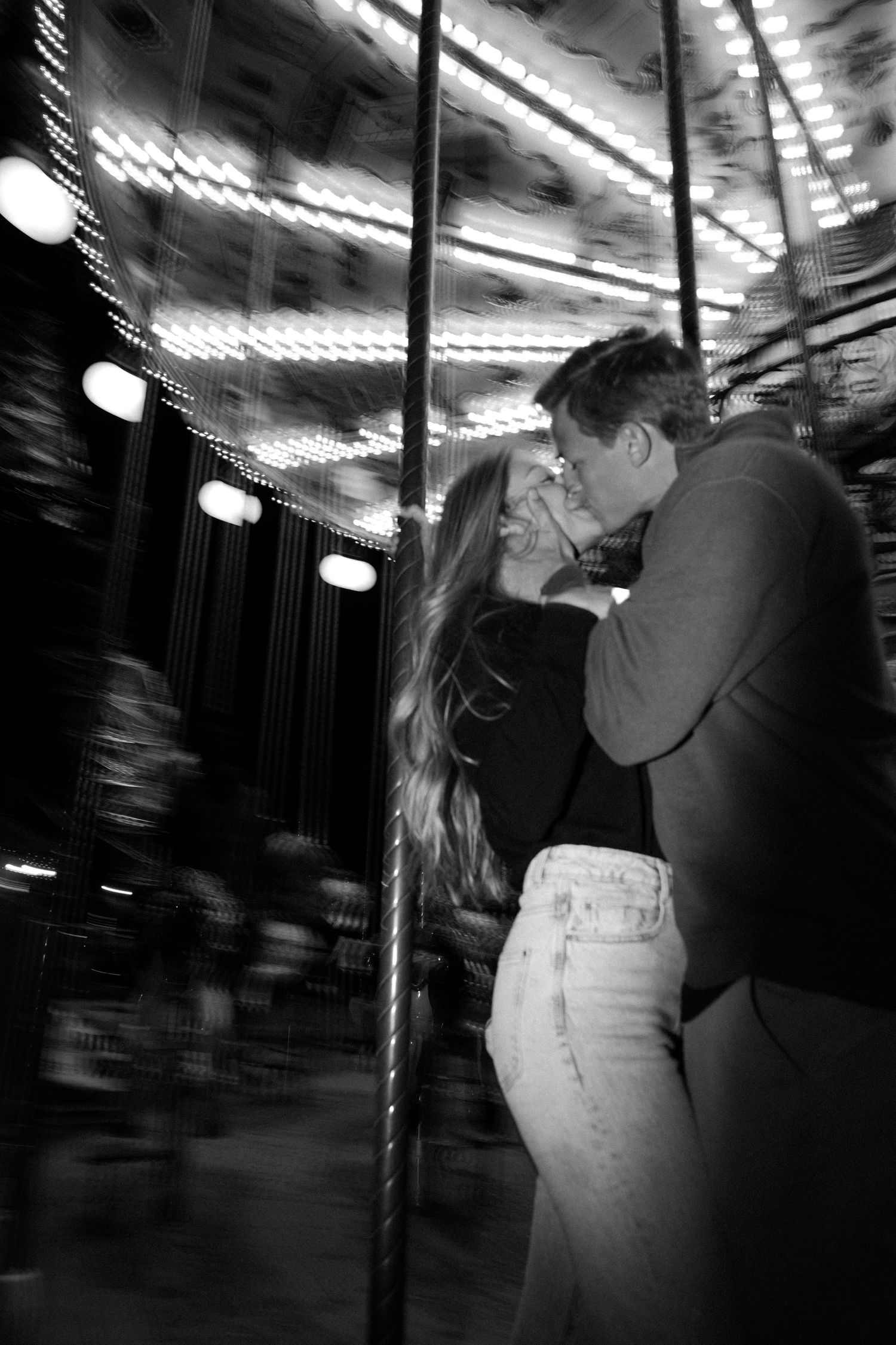 Romantic silhouette of couple embracing on a carousel with glowing lights in black and white.