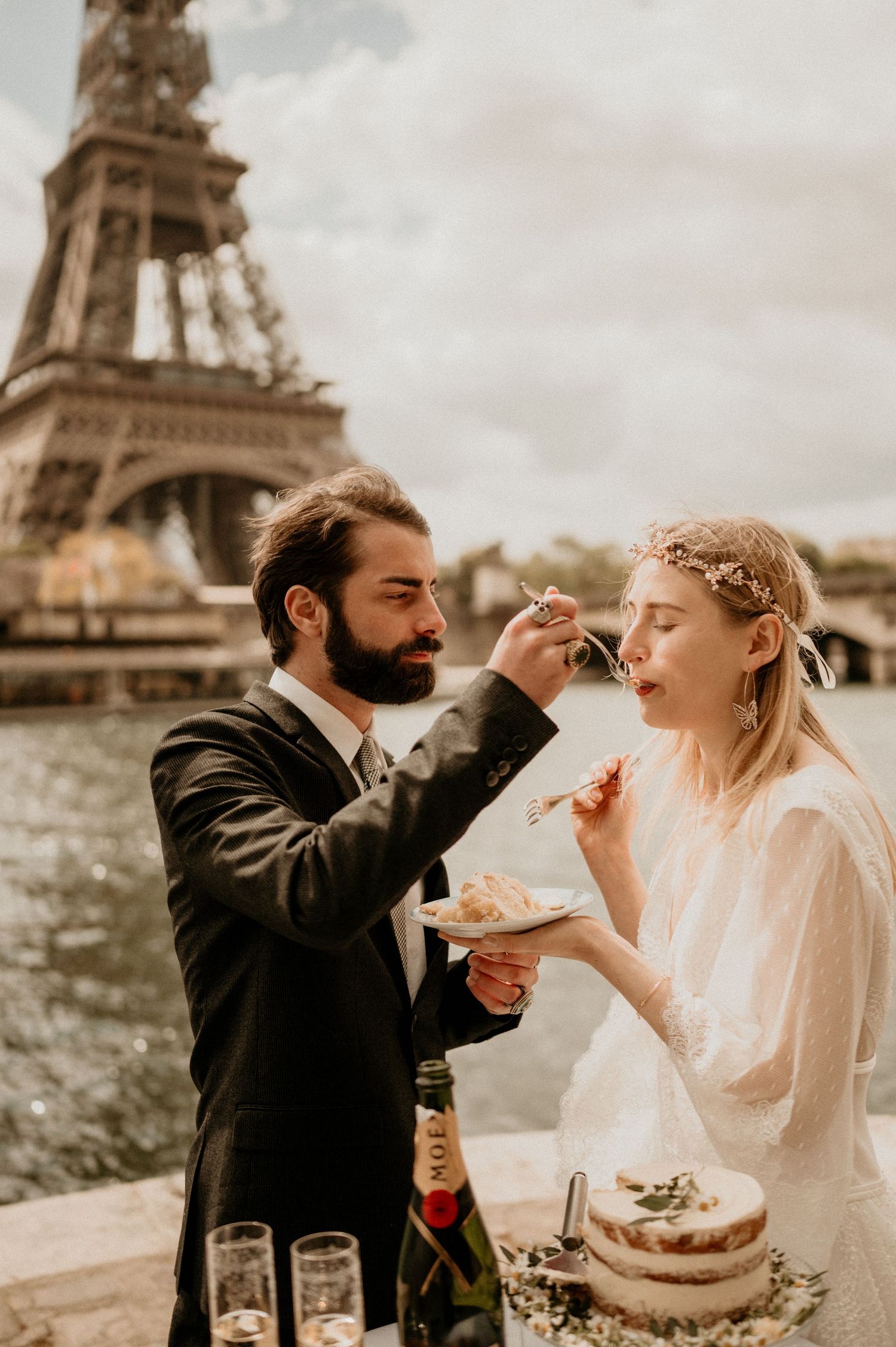 A tender moment of cake sharing between newlyweds with the Eiffel Tower in the background.