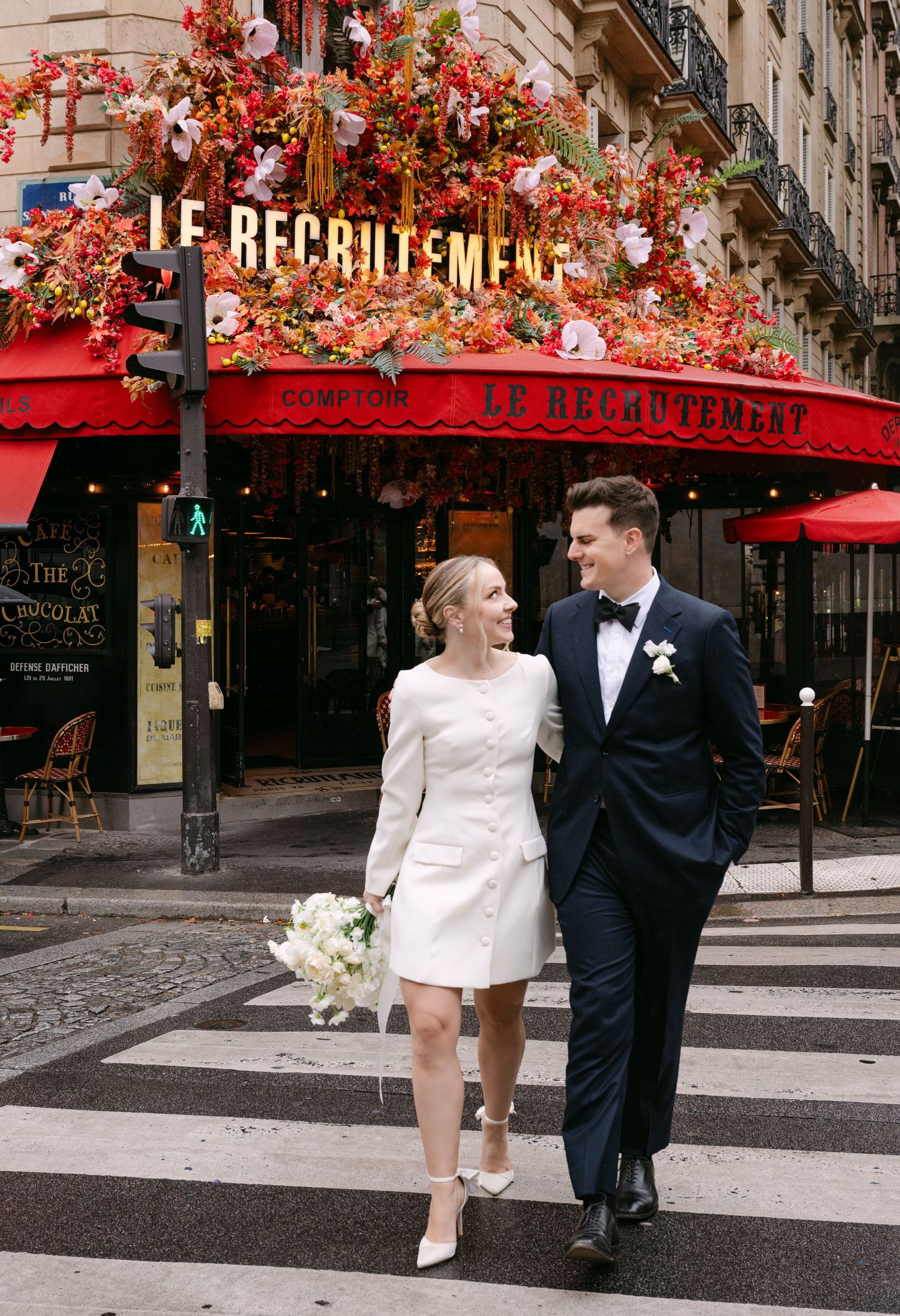 Elegant couple walking outside Le Republican cafe in Paris with festive red decor.