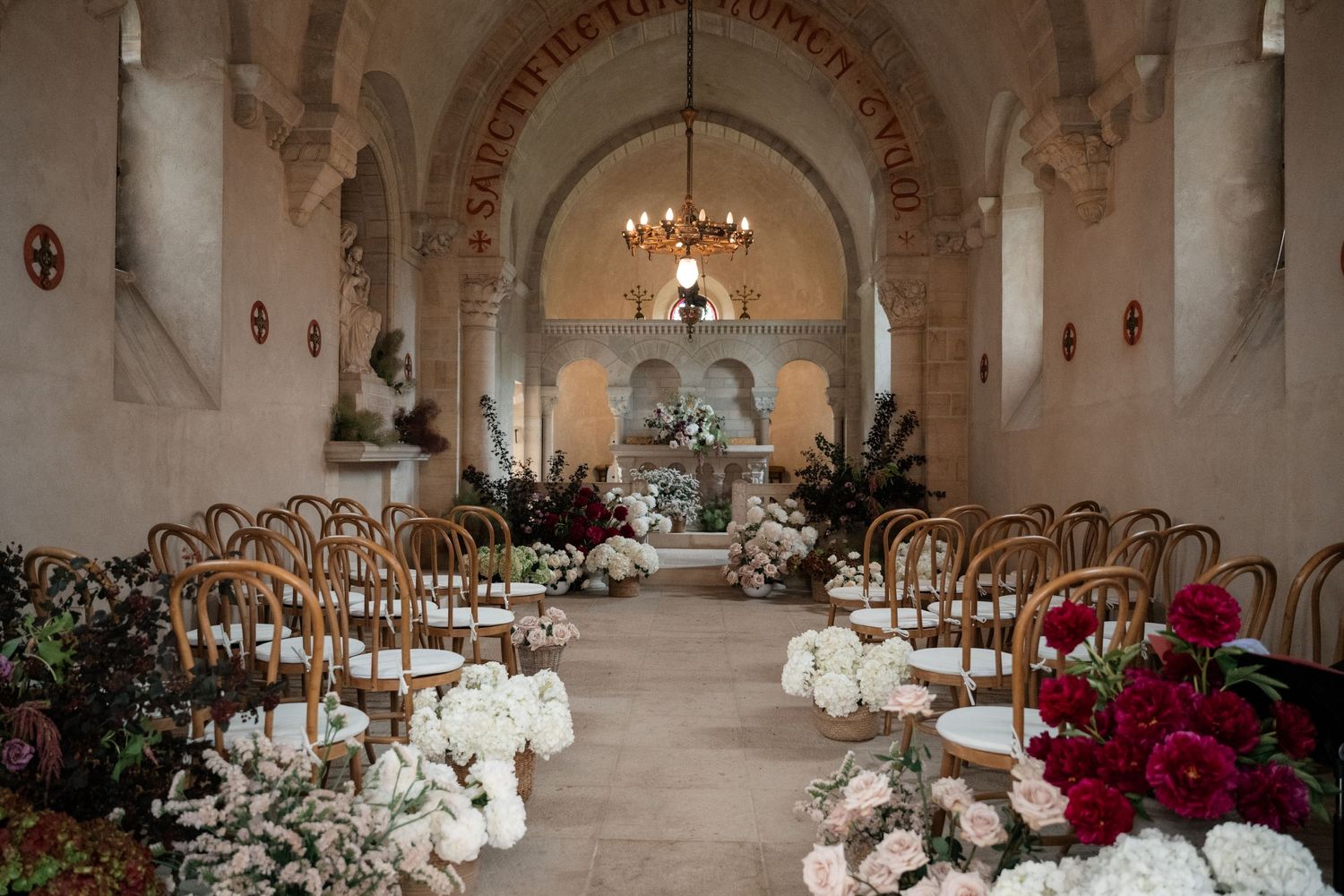 Elegant wedding reception setup in a white stone castle ballroom with crystal chandeliers and floral centerpieces.