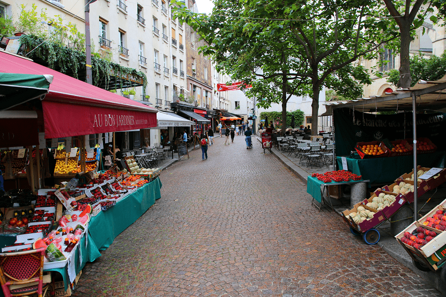 Bustling Parisian market street with vendors selling fresh produce under red awnings.