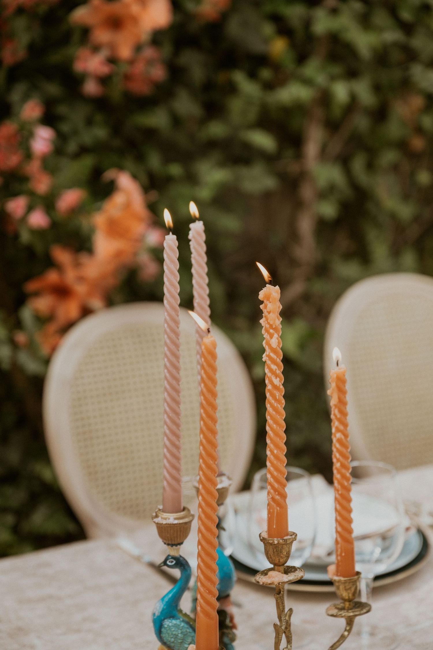 Elegant outdoor wedding table with twisted taper candles in gold candleholders and a teal peacock figurine.