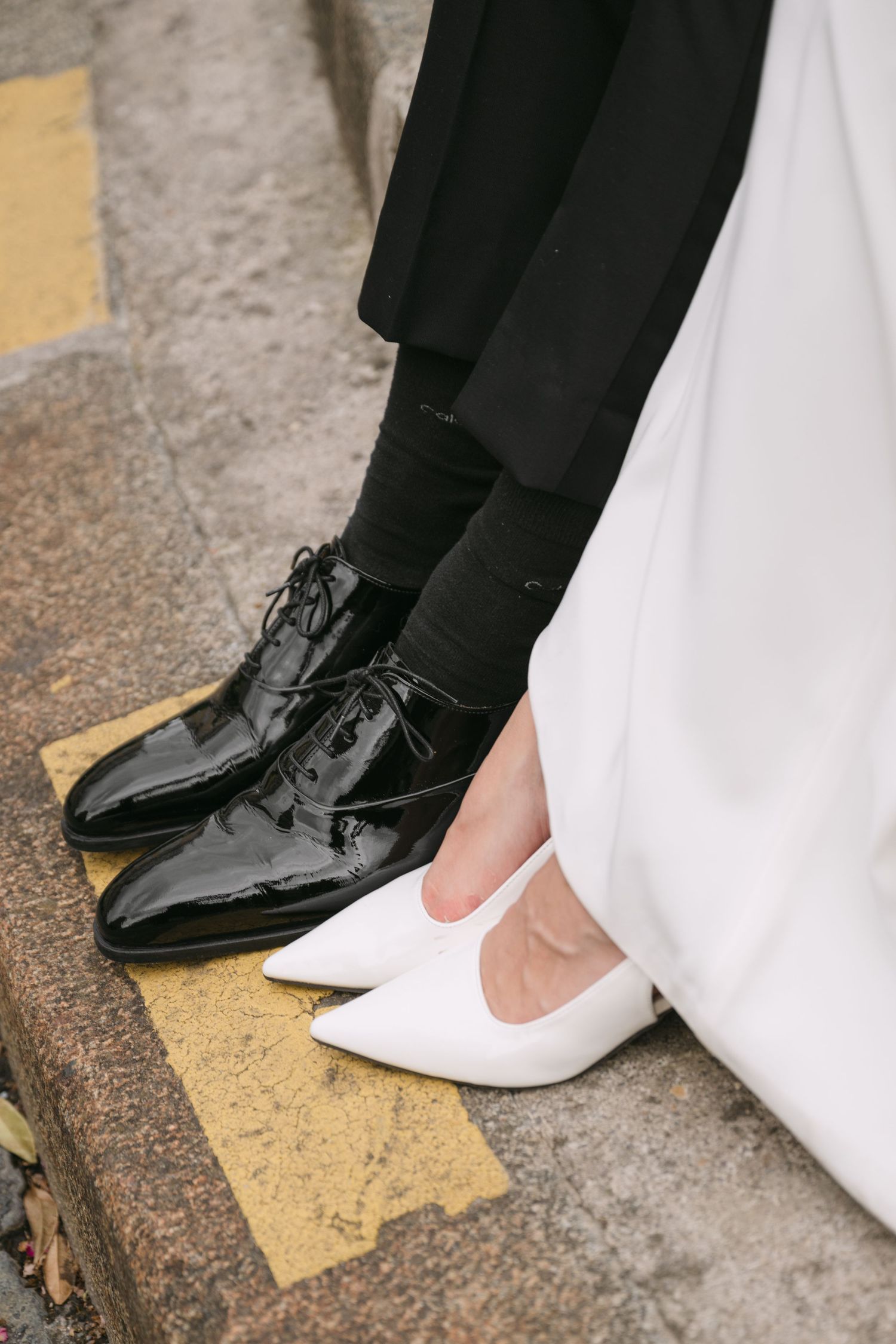 Close-up of bride in white heels and groom in black patent leather shoes standing on stone steps.
