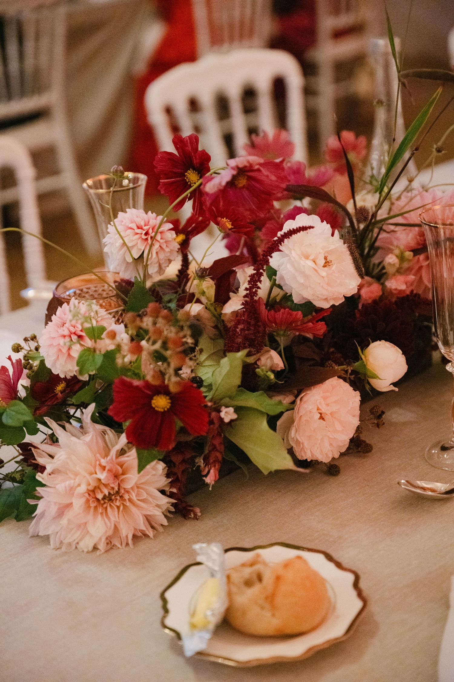 Lush wedding centerpiece with pink dahlias, red cosmos, and garden roses on a linen tablecloth.