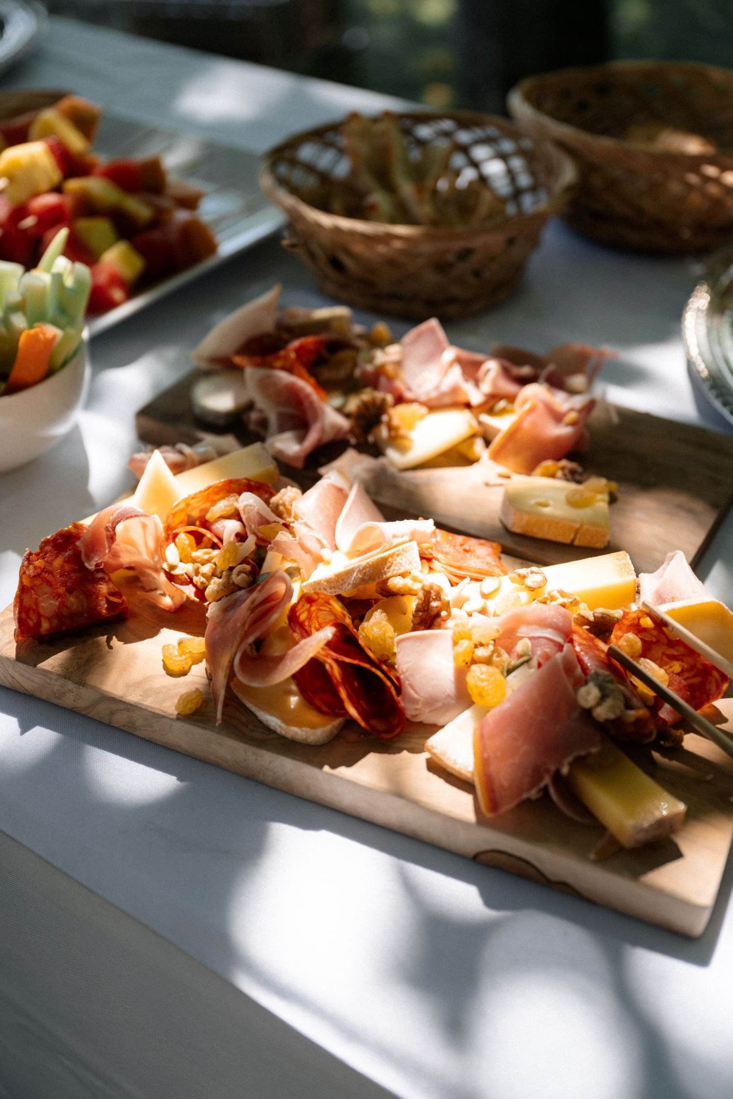 Rustic charcuterie board with prosciutto, cheese, and nuts on a sunlit outdoor catering table.