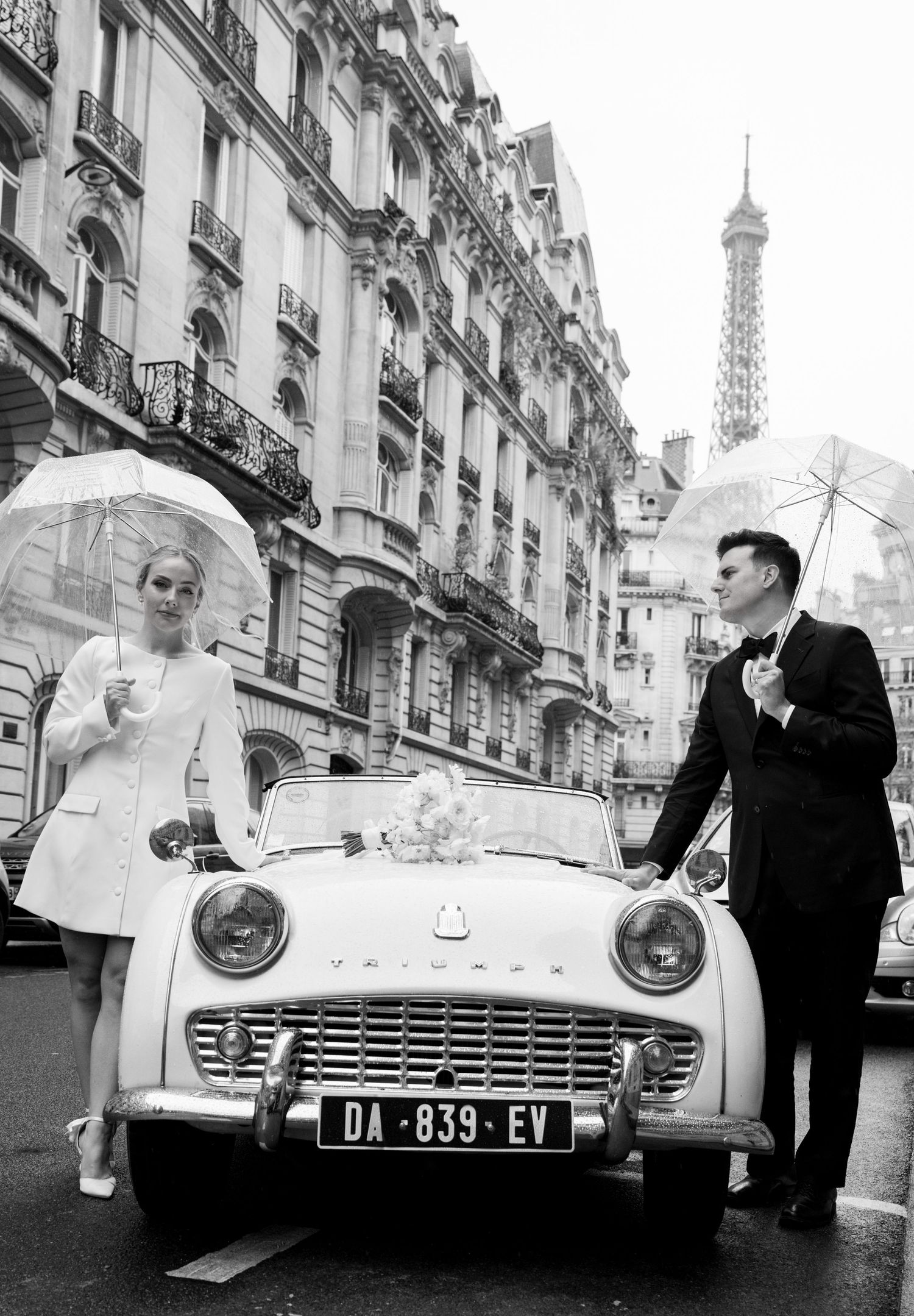 Vintage black and white photograph of a classic Triumph TR3 car parked on a Parisian street with the Eiffel Tower visible.