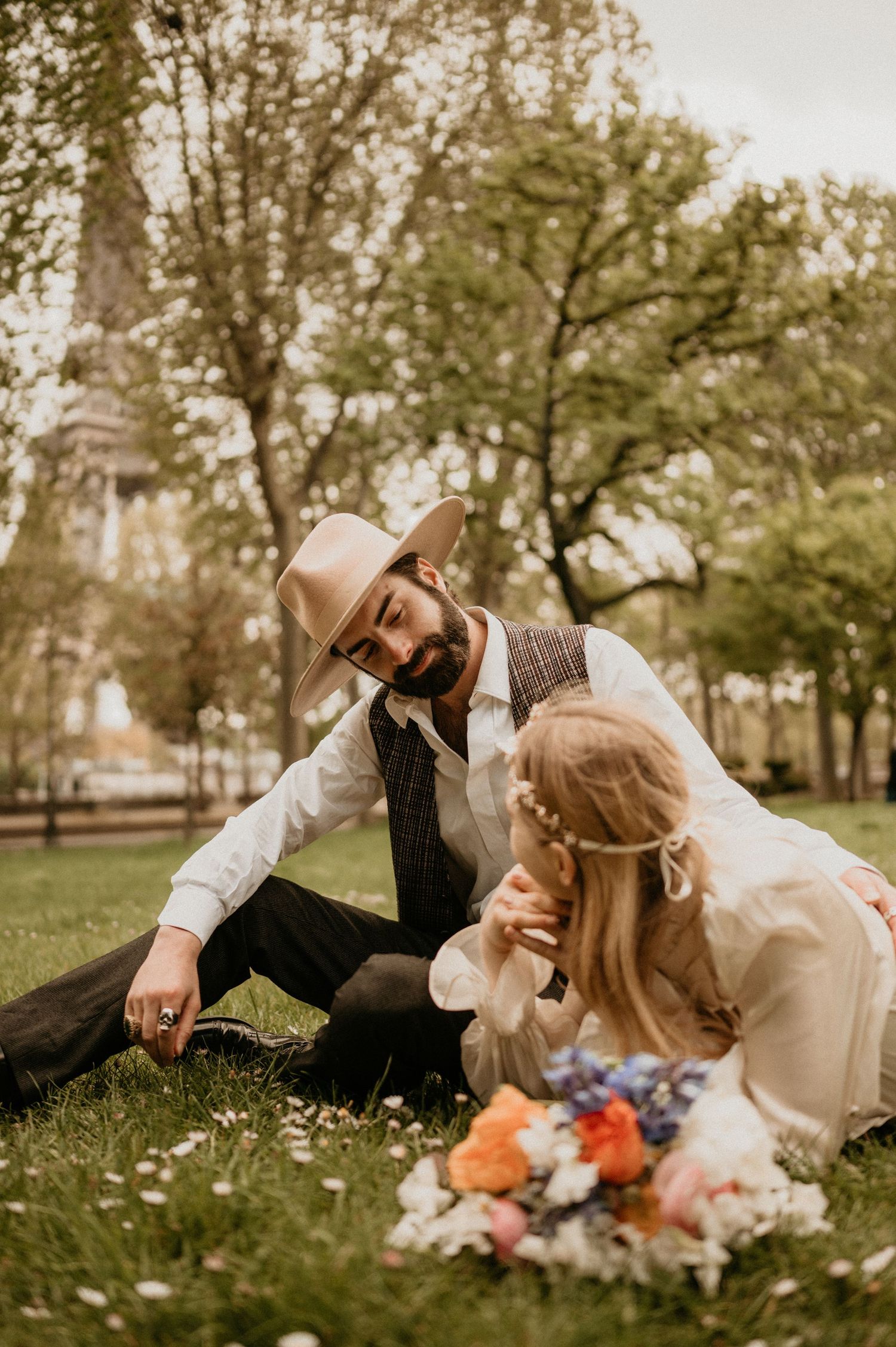 Vintage-styled couple sharing tender moment on grass with spring flowers in Paris park.