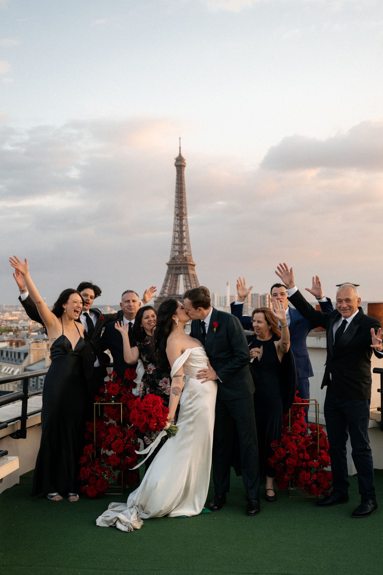 Wedding party celebrates with joyful poses against Paris skyline with Eiffel Tower at sunset.
