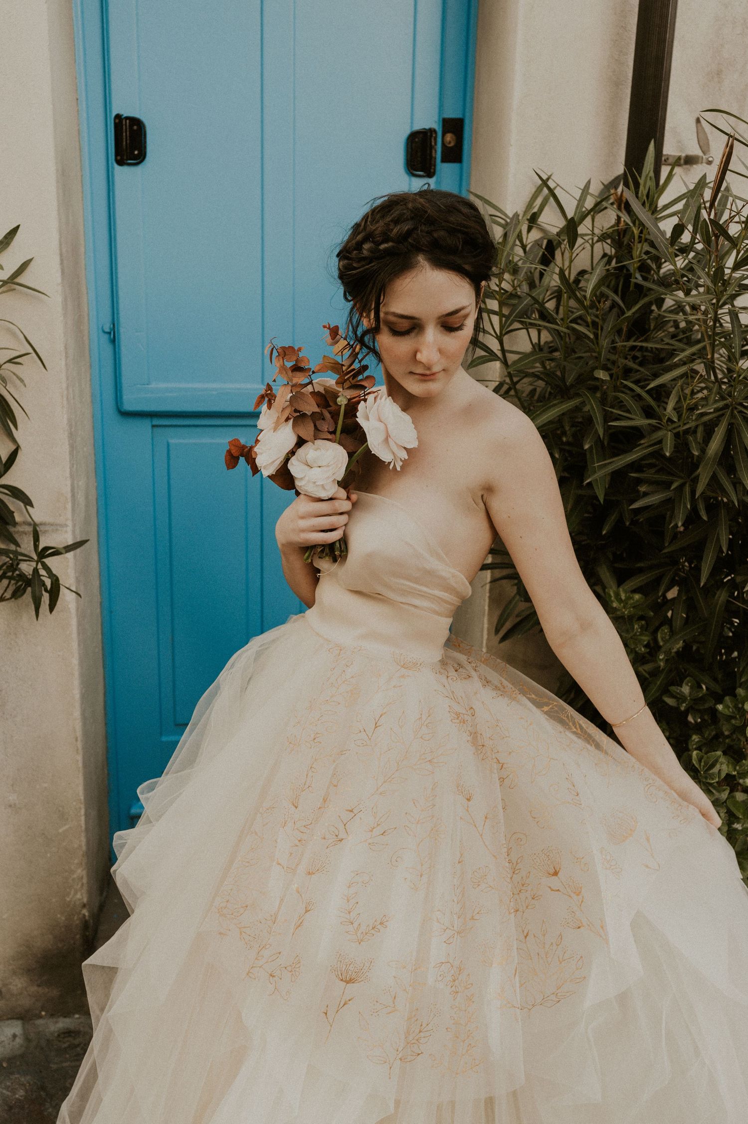 A romantic bridal photo featuring a strapless ball gown and floral bouquet against a turquoise door.