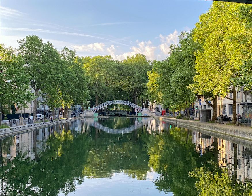 Picturesque canal in Paris with a stone bridge and tree-lined banks reflecting in calm waters.