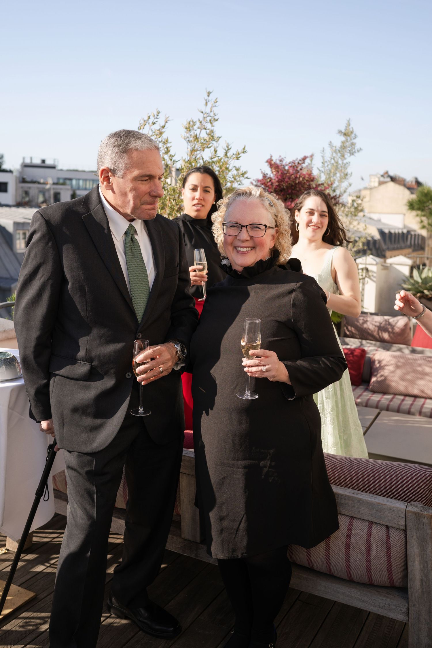 Elegantly dressed couples enjoying champagne on a Parisian rooftop terrace at golden hour.