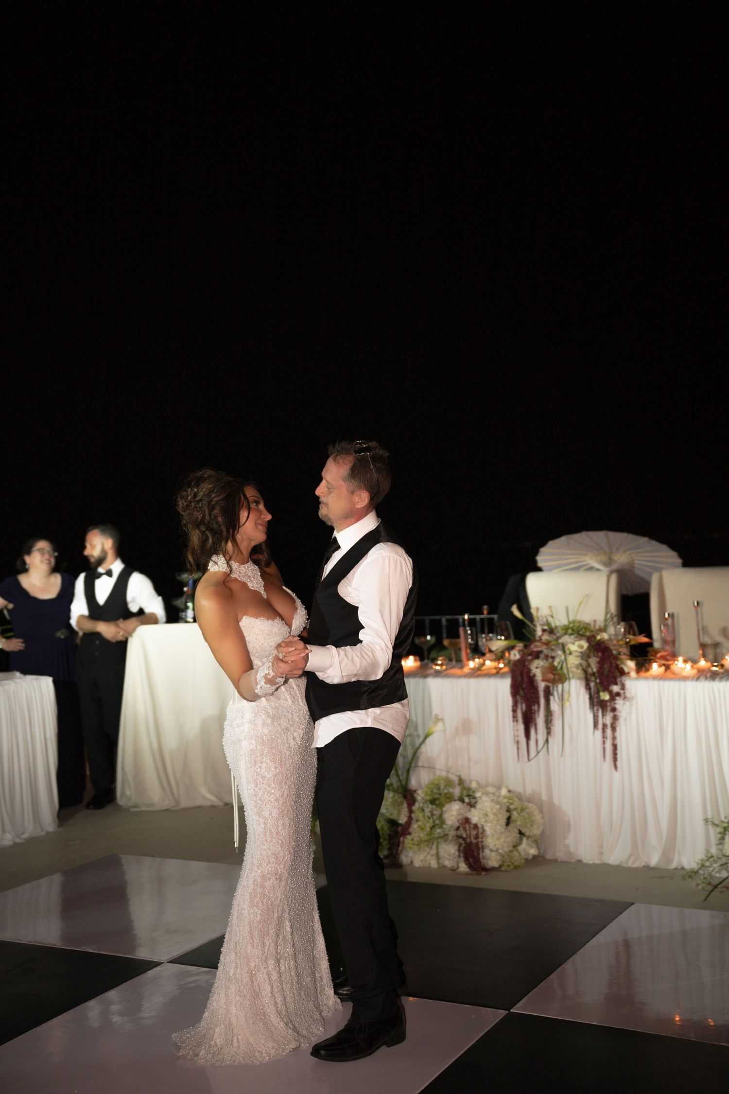 Bride and groom share first dance on checkered floor at elegant outdoor night wedding.