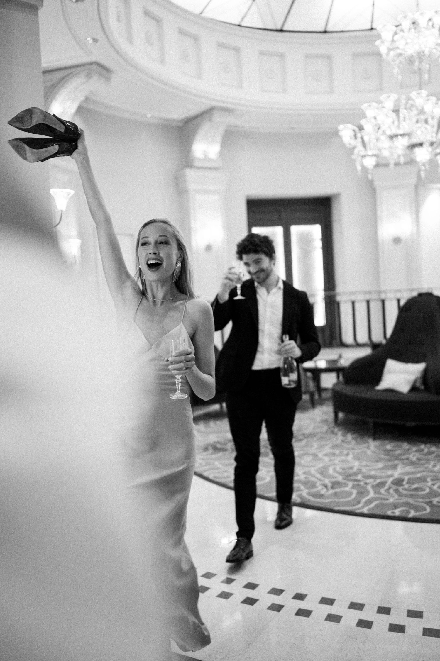 Black and white photo of a joyful couple celebrating with champagne in an elegant ballroom venue.