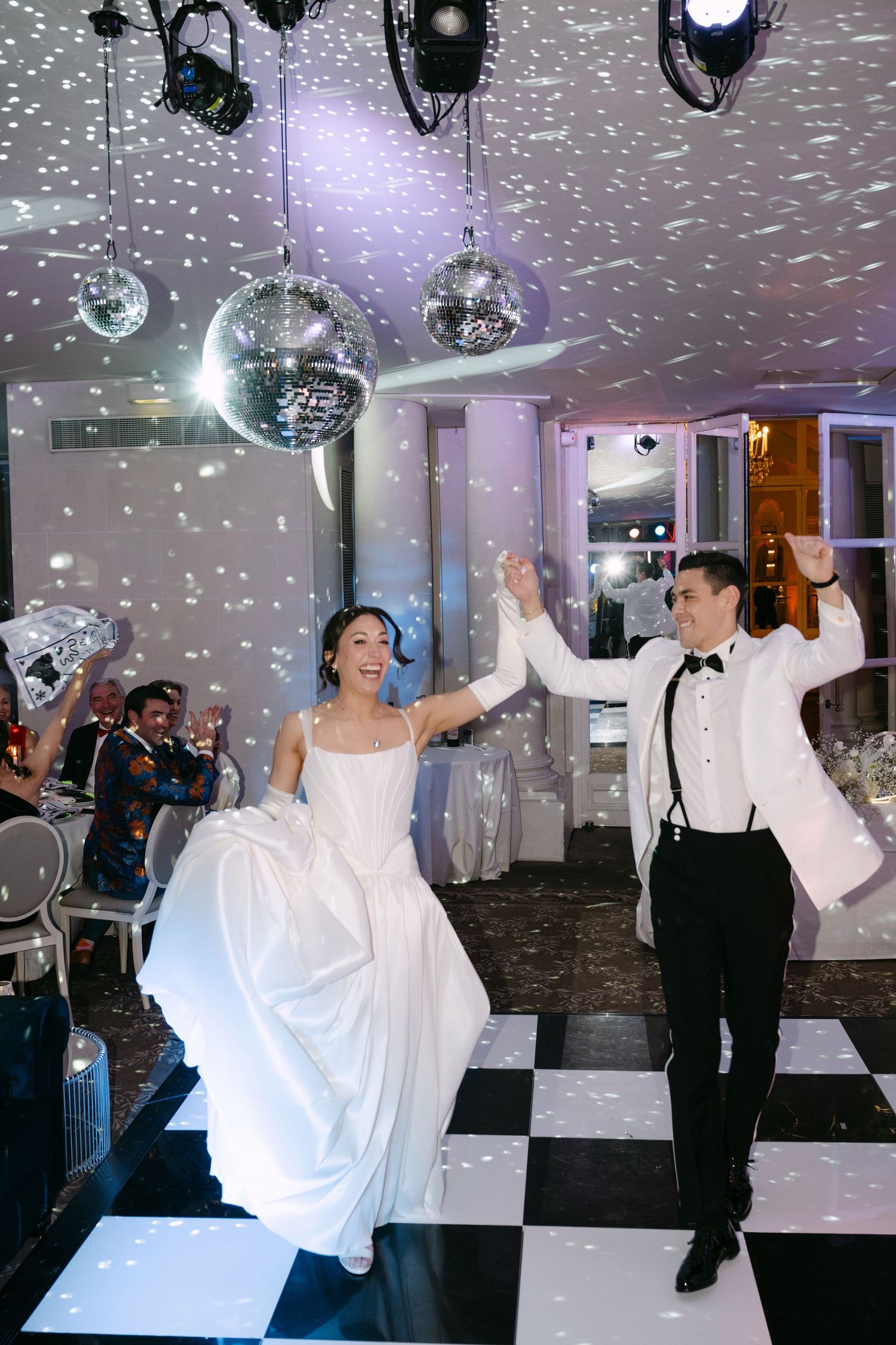 Bride and groom making grand entrance onto black and white checkered dance floor with confetti falling.