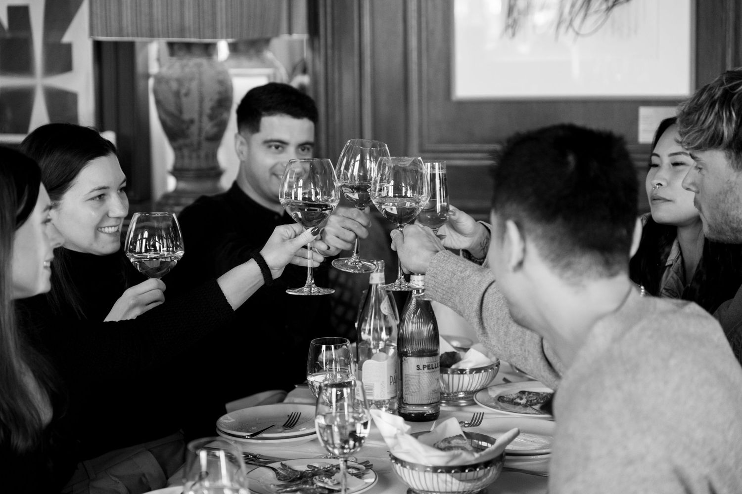 Group of friends toasting with red wine glasses at restaurant dinner in black and white.