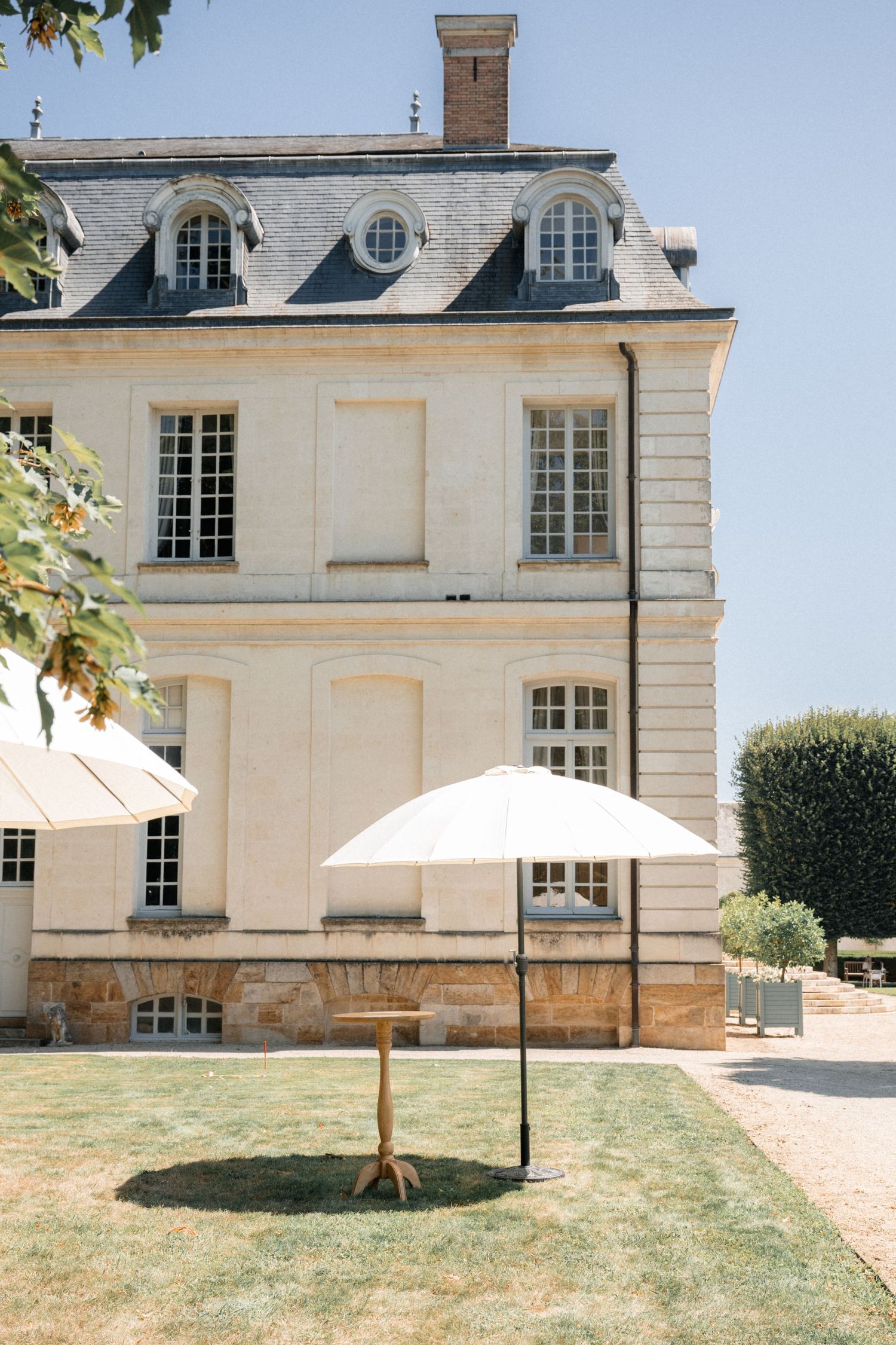 Elegant French chateau exterior with white patio umbrella on manicured lawn under clear blue sky.