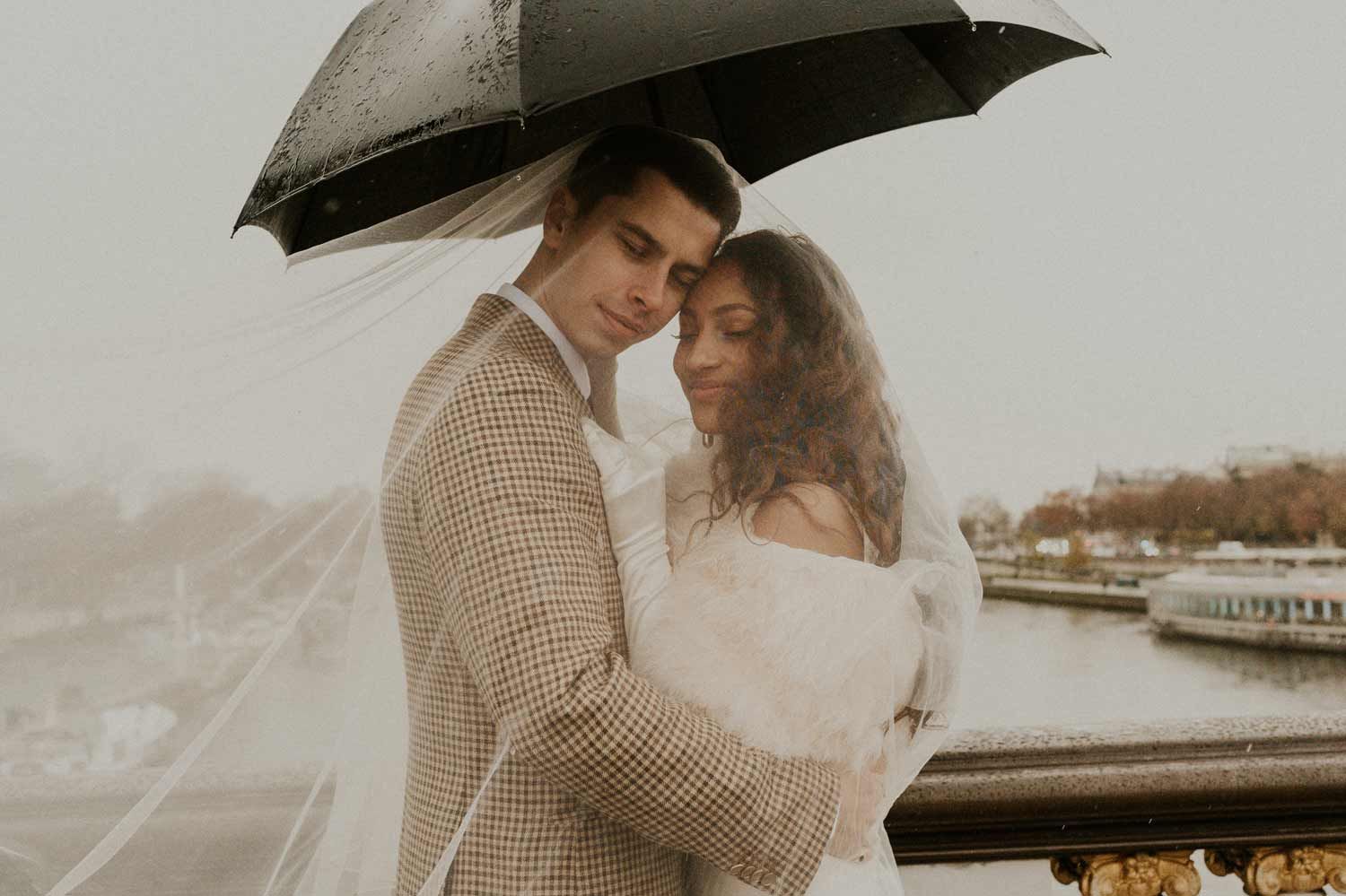 A romantic rainy day portrait of a couple sharing an intimate moment by a stone balcony.