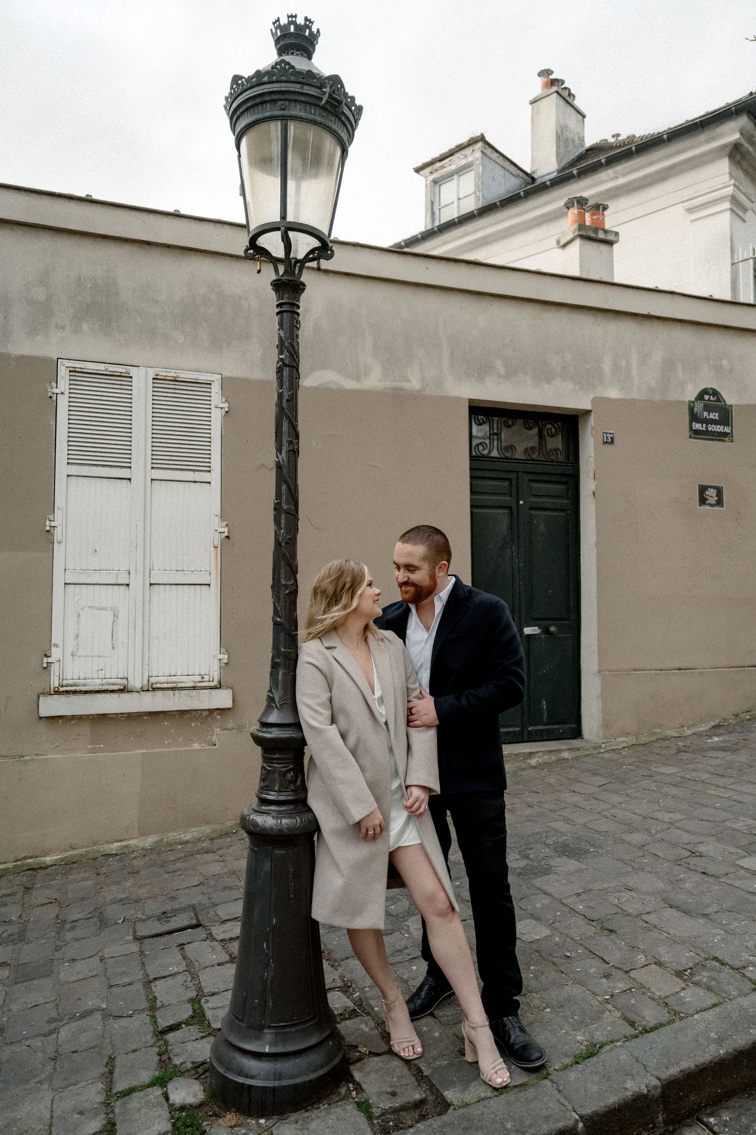 A romantic couple poses against a vintage lamp post on a cobblestone street in Paris.