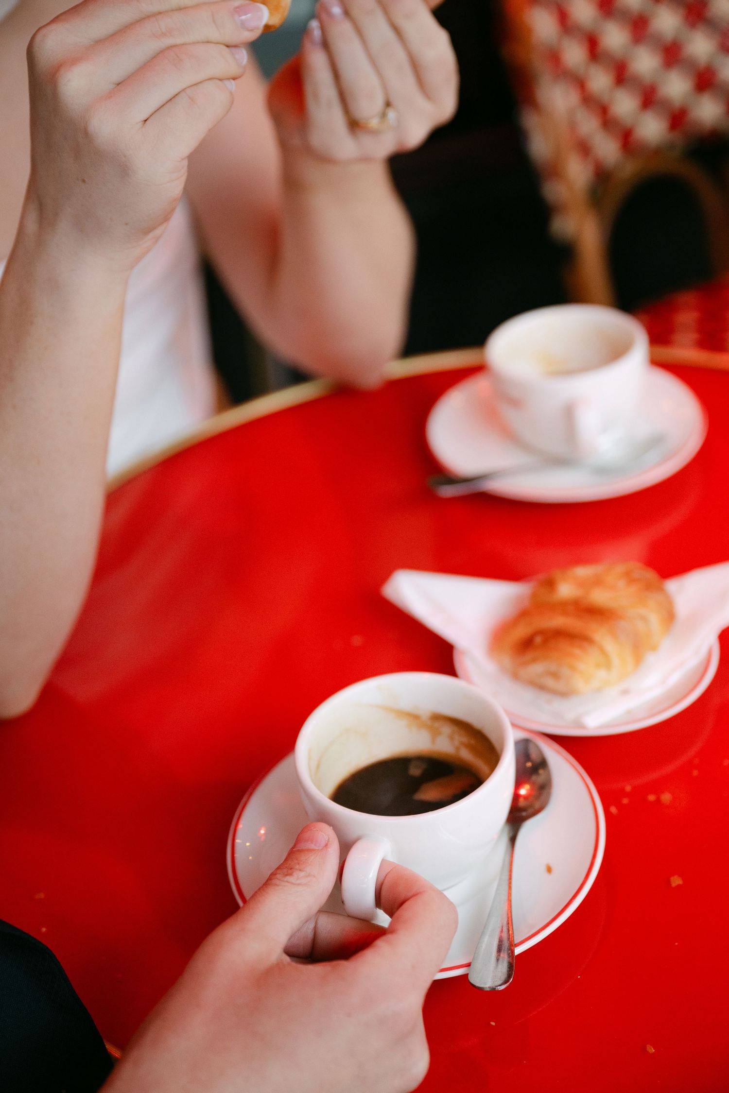 Close-up sequence of hands holding white coffee cups on a red tablecloth.