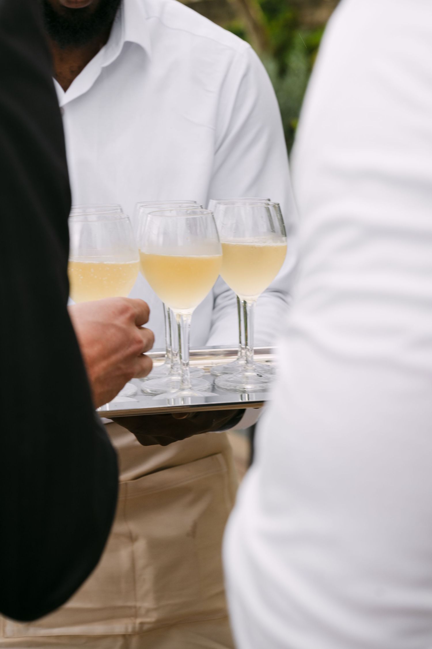 A server carries a tray with three glasses of white wine in elegant stemware.