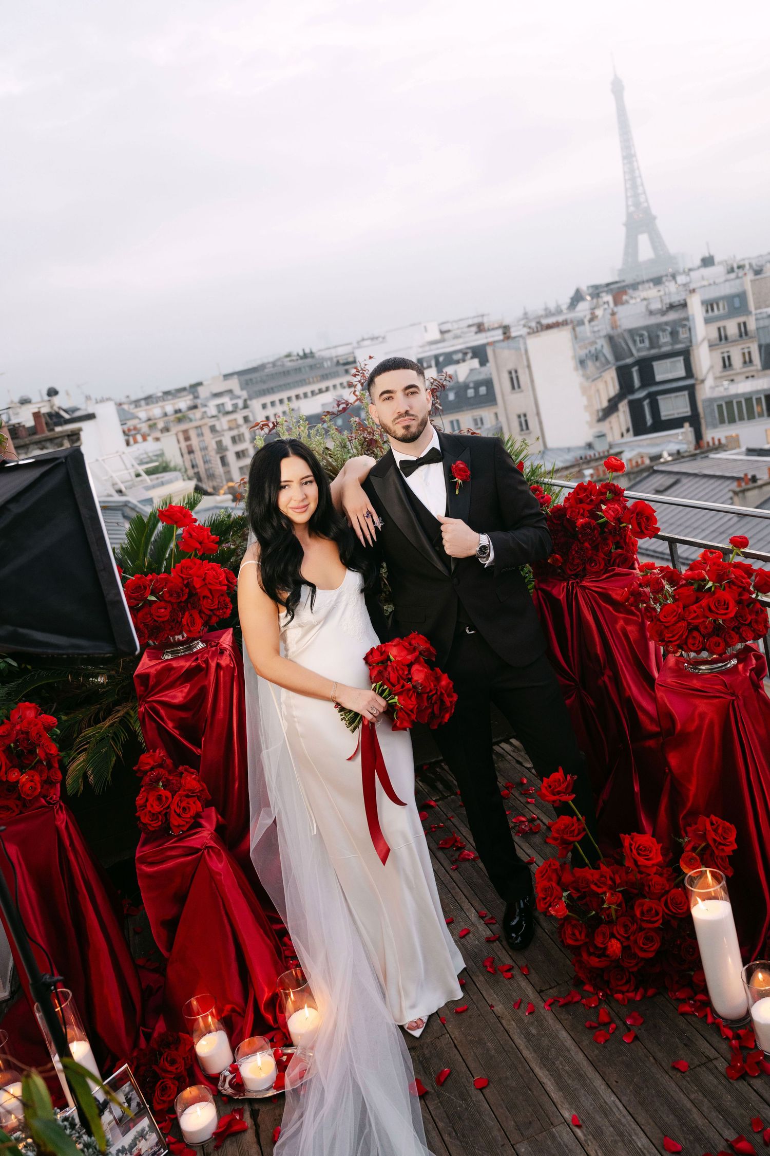 Elegant couple posing with red roses and candles on Paris rooftop with Eiffel Tower backdrop.