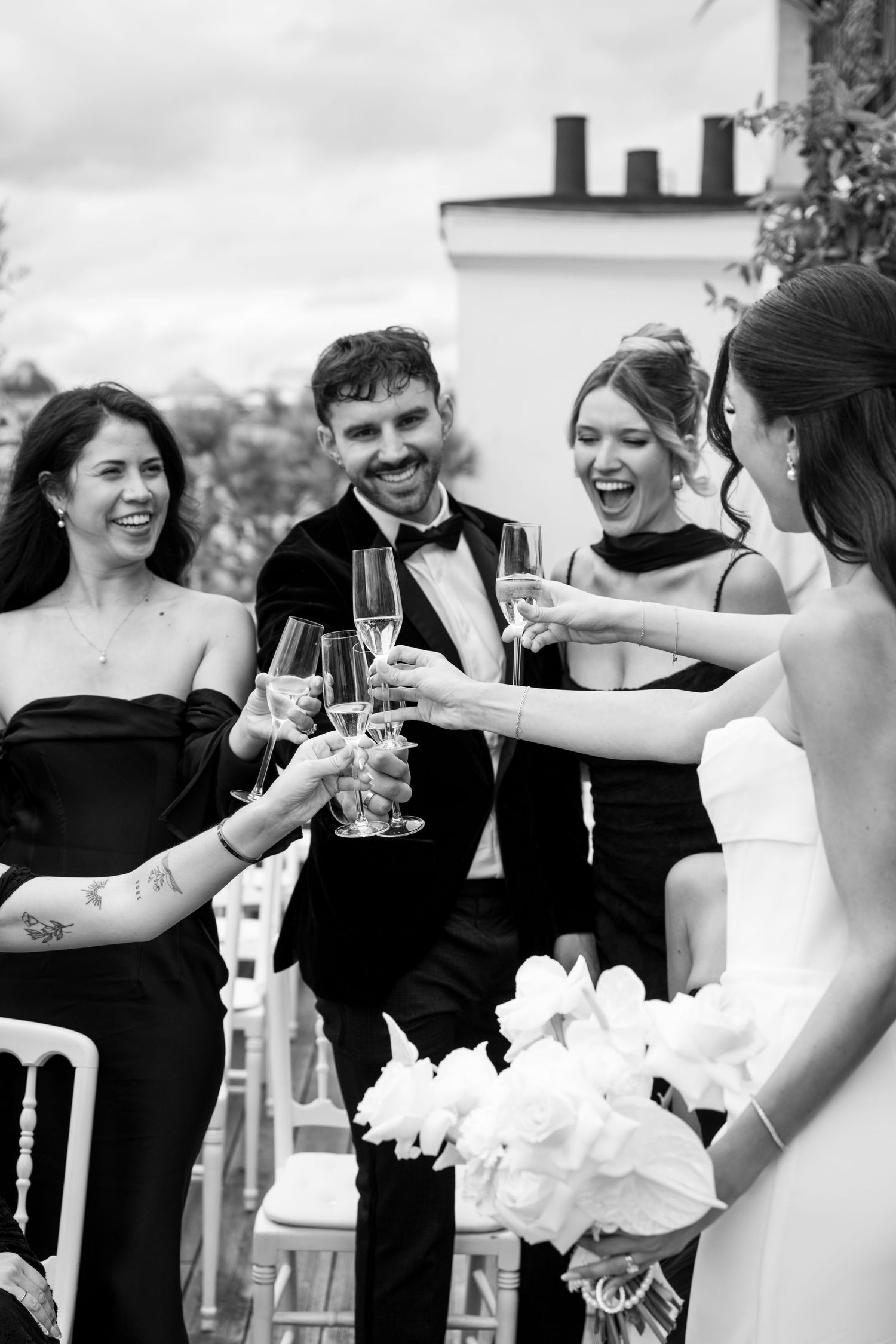 Black and white photo of bride and guests toasting with champagne glasses at outdoor wedding reception.