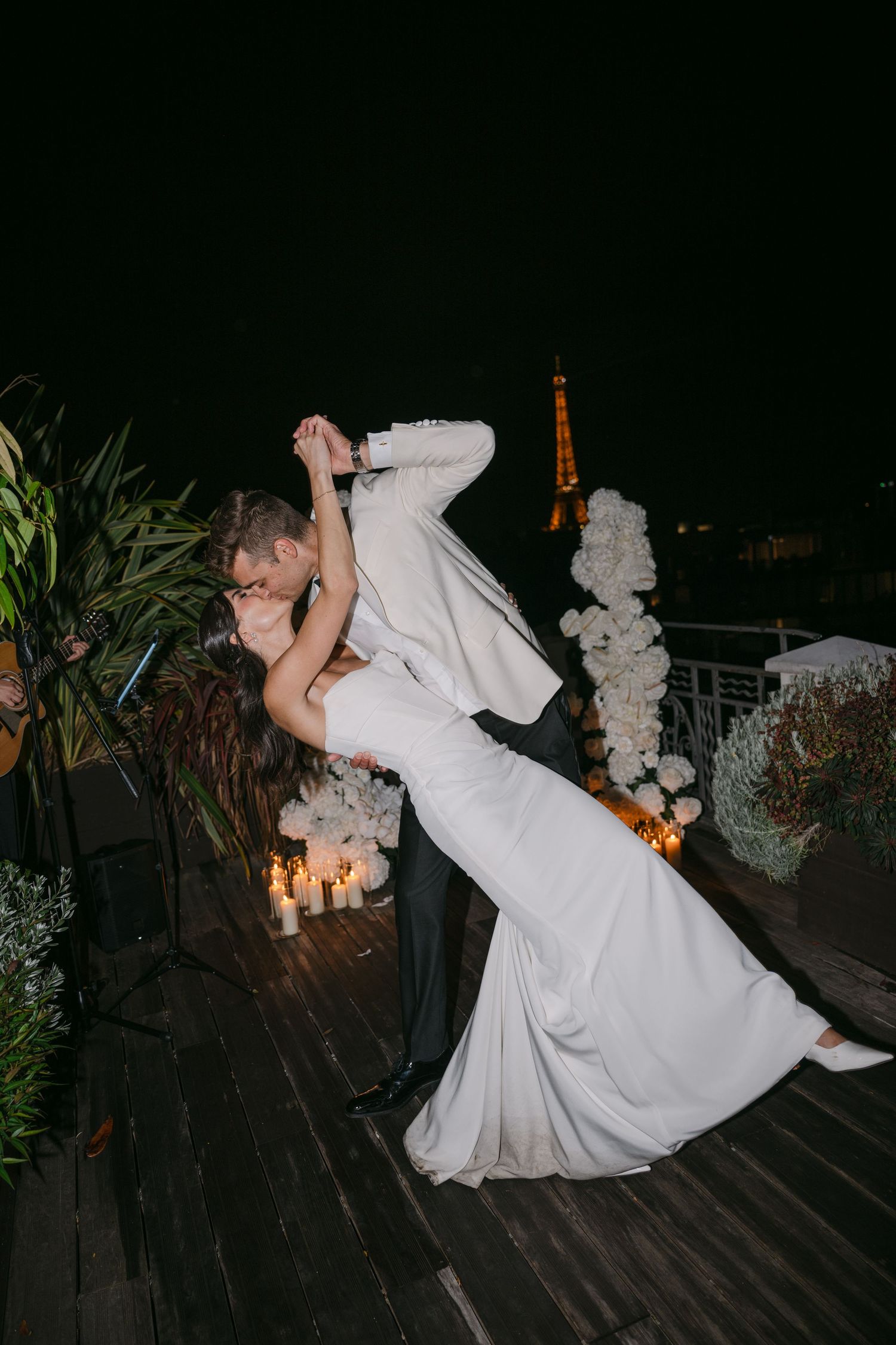 Bride and groom sharing a romantic dip kiss on a rooftop with Eiffel Tower backdrop.