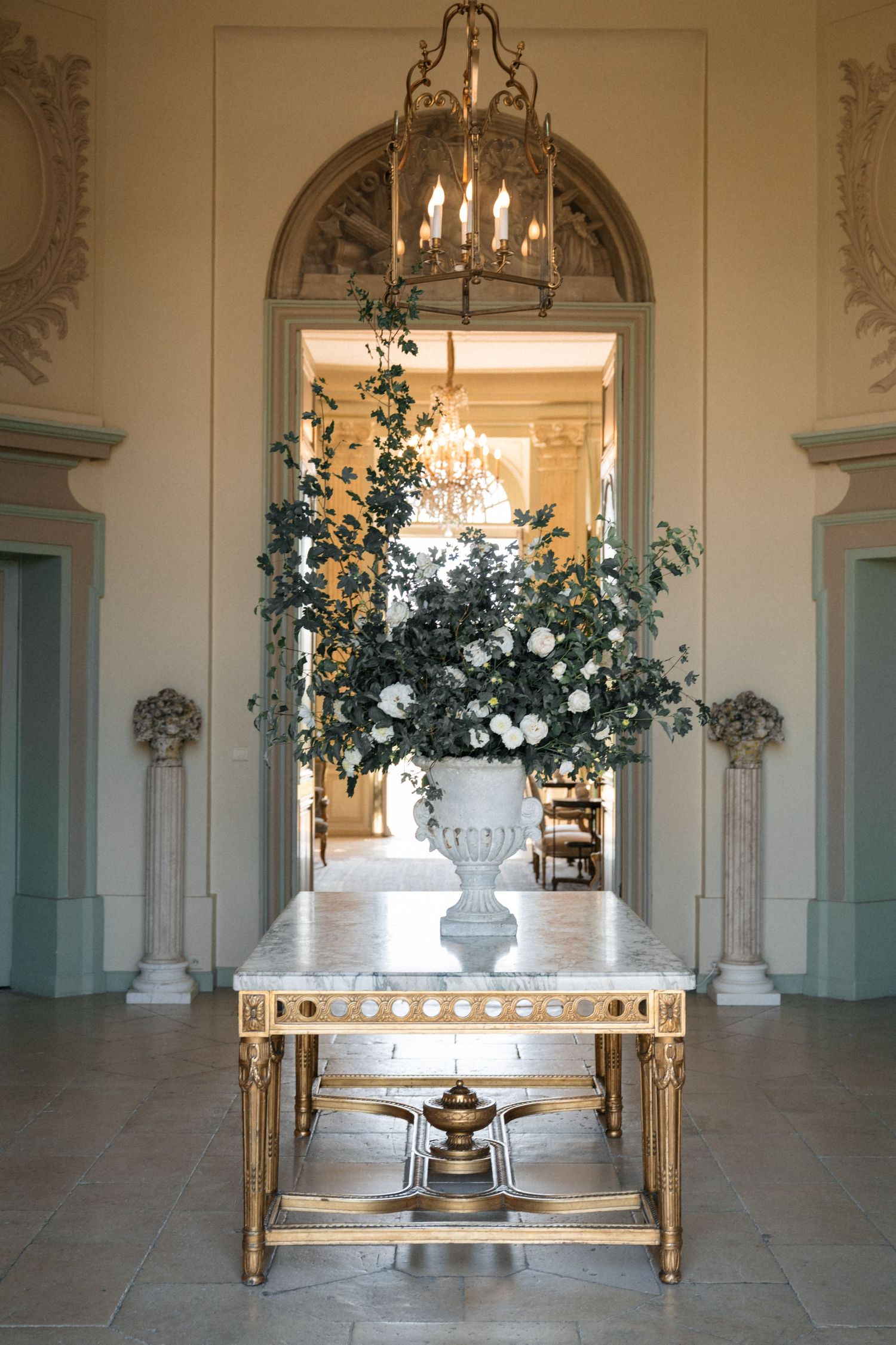 Elegant marble-topped gilded console table with white floral arrangement in ornate interior.