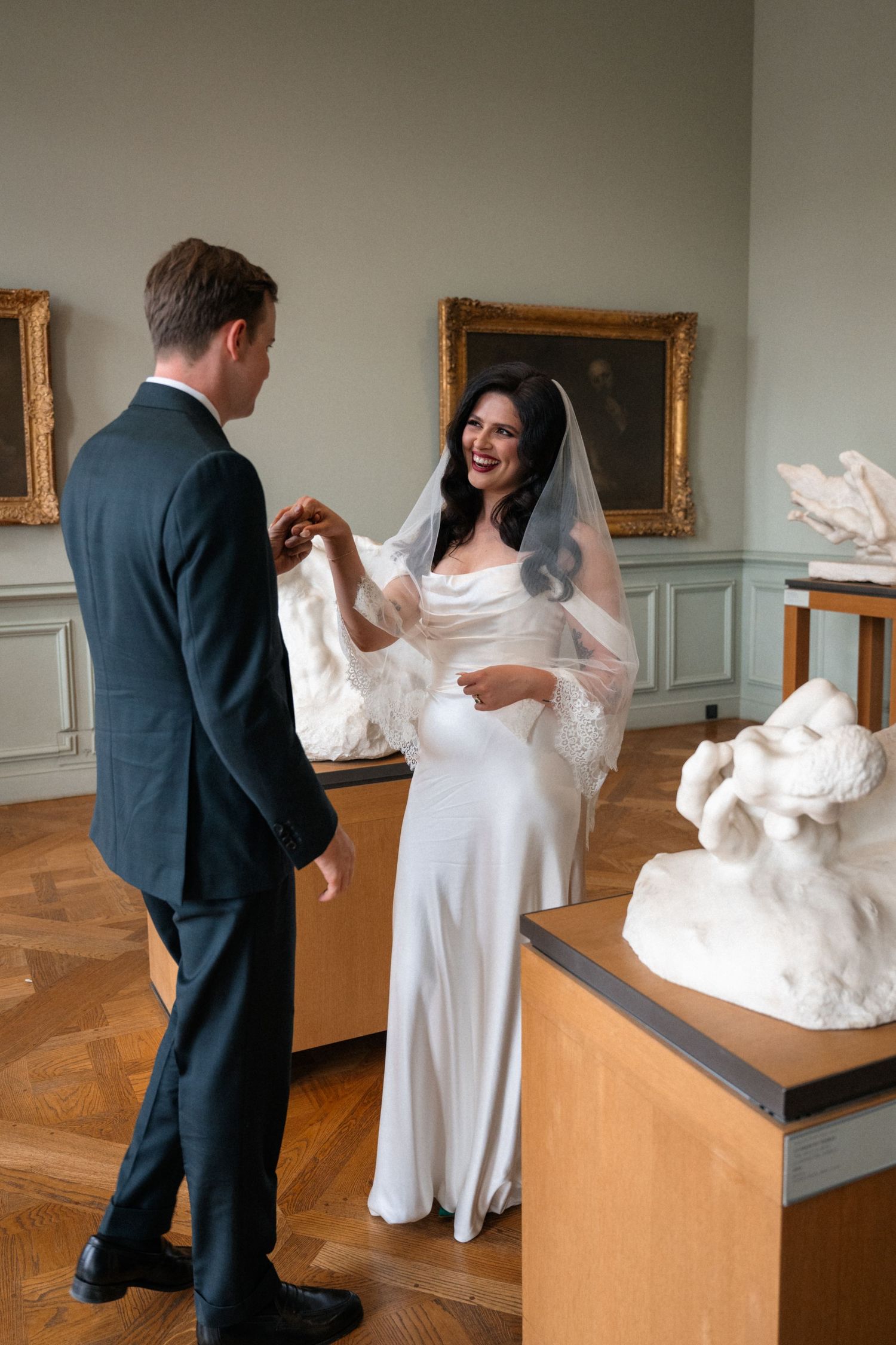 Bride and groom sharing a joyful moment in an elegant museum gallery.