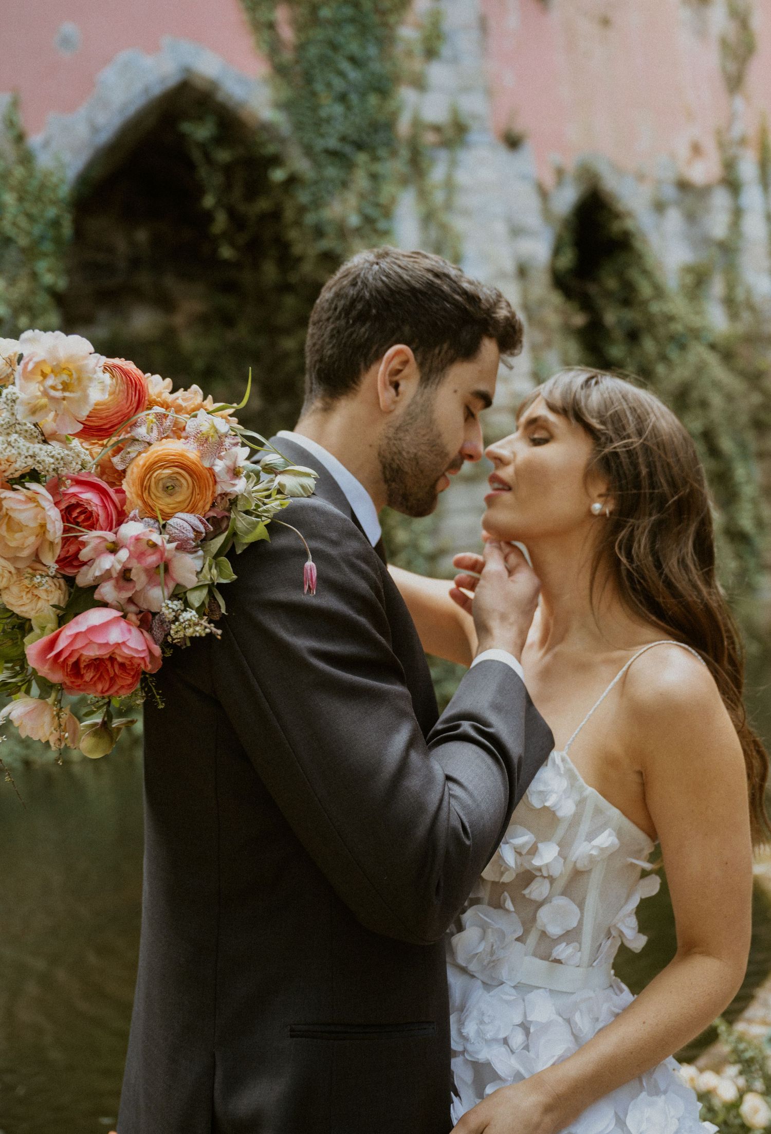 Groom tenderly holds bride's chin as they share an intimate moment with a colorful bridal bouquet.