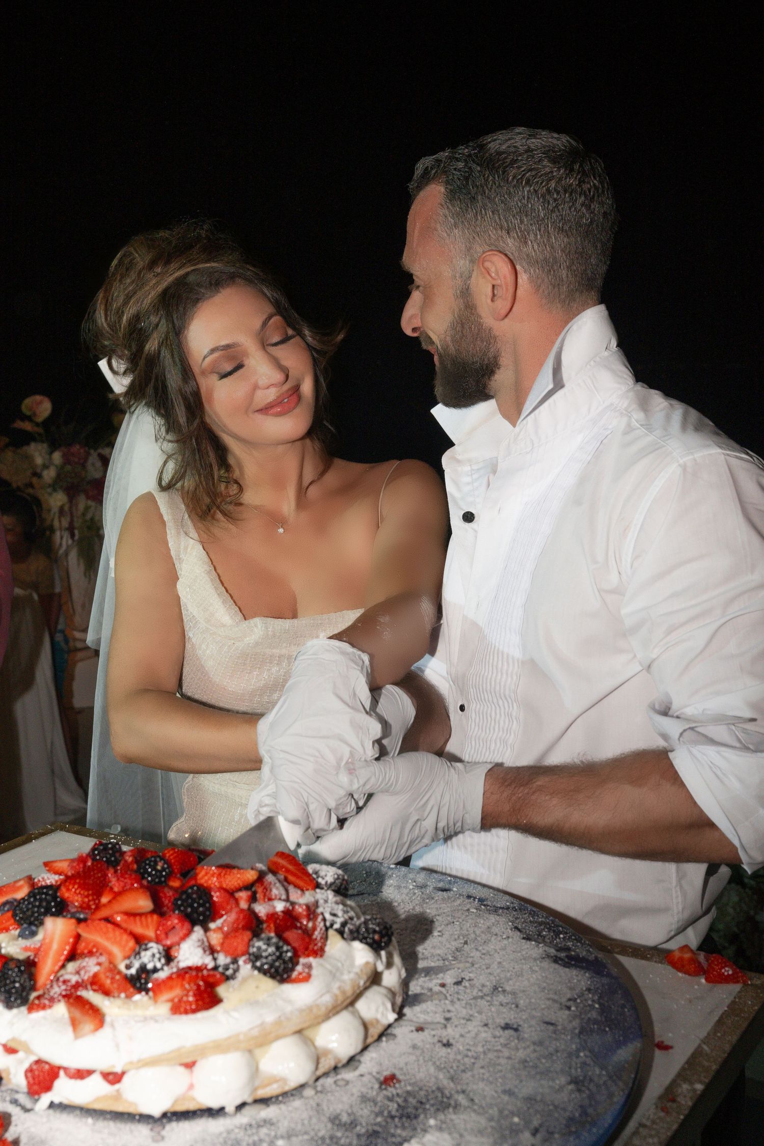 Bride and groom sharing a tender moment while cutting their elegant fruit-topped wedding cake decorated with fresh berries.