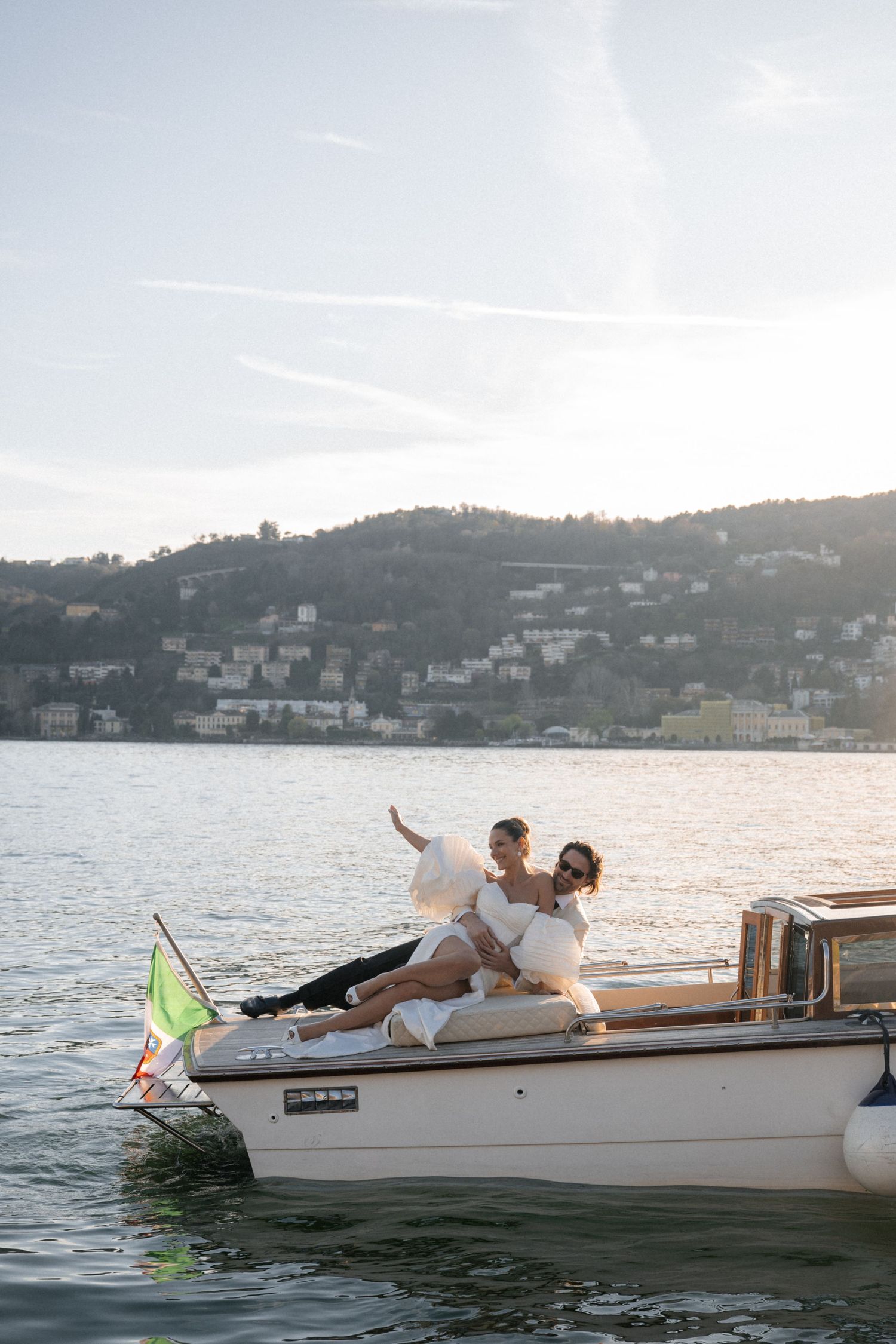 Joyful newlyweds posing on bow of boat at sunset on Lake Como, Italy.