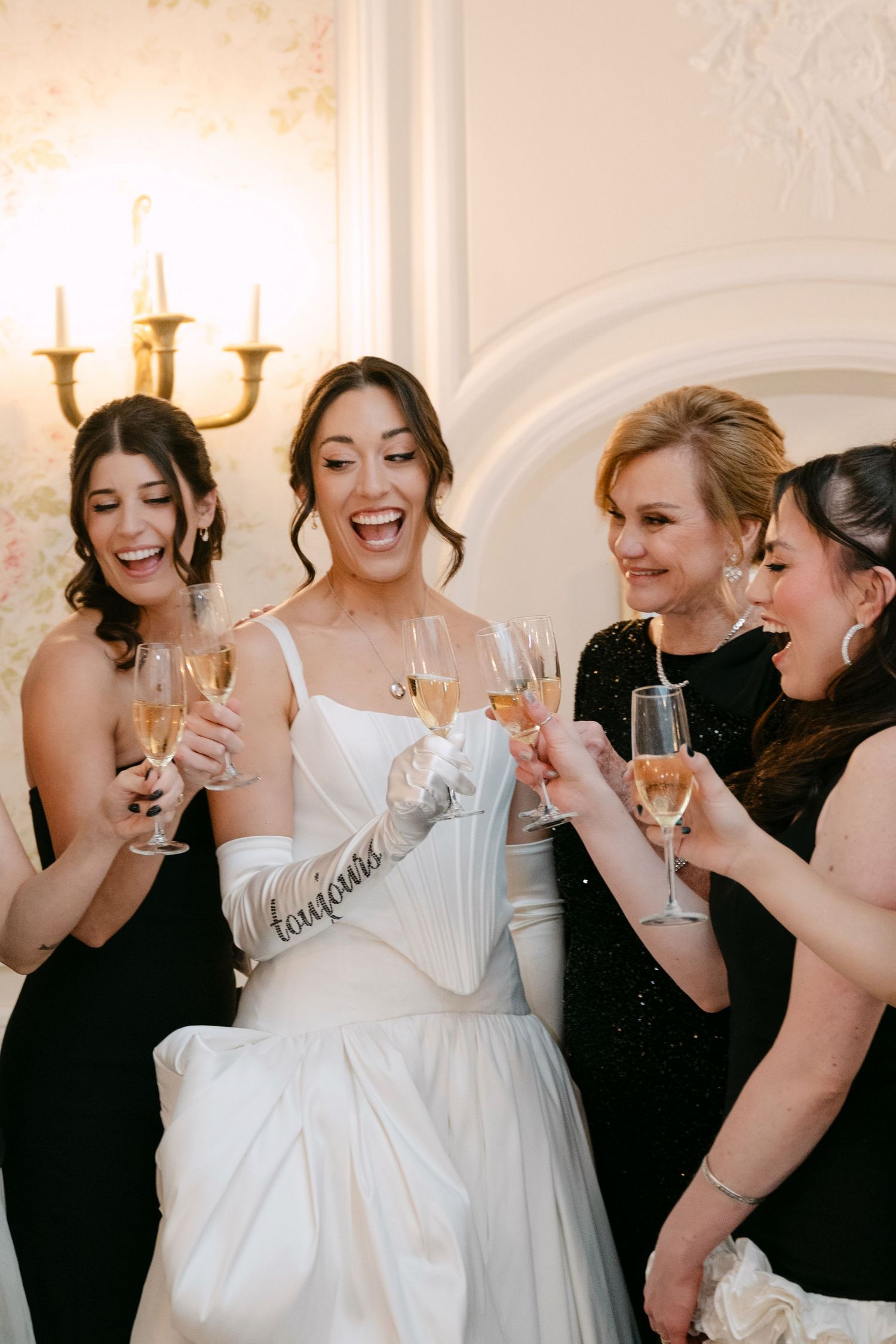 Bride and bridesmaids in black dresses toasting with champagne glasses at a wedding celebration.
