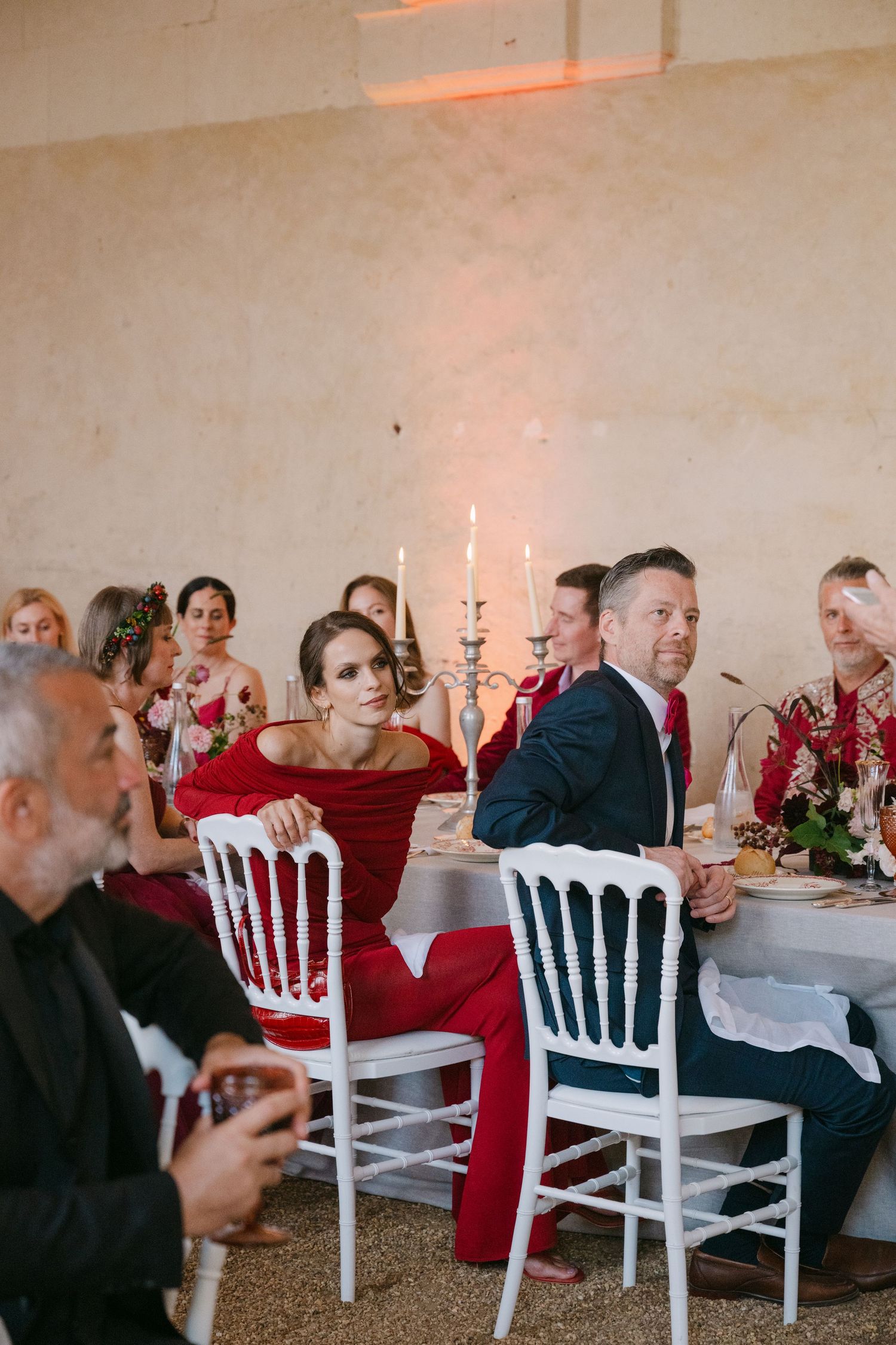 Wedding guests listening to speeches at a candlelit reception in a white venue.