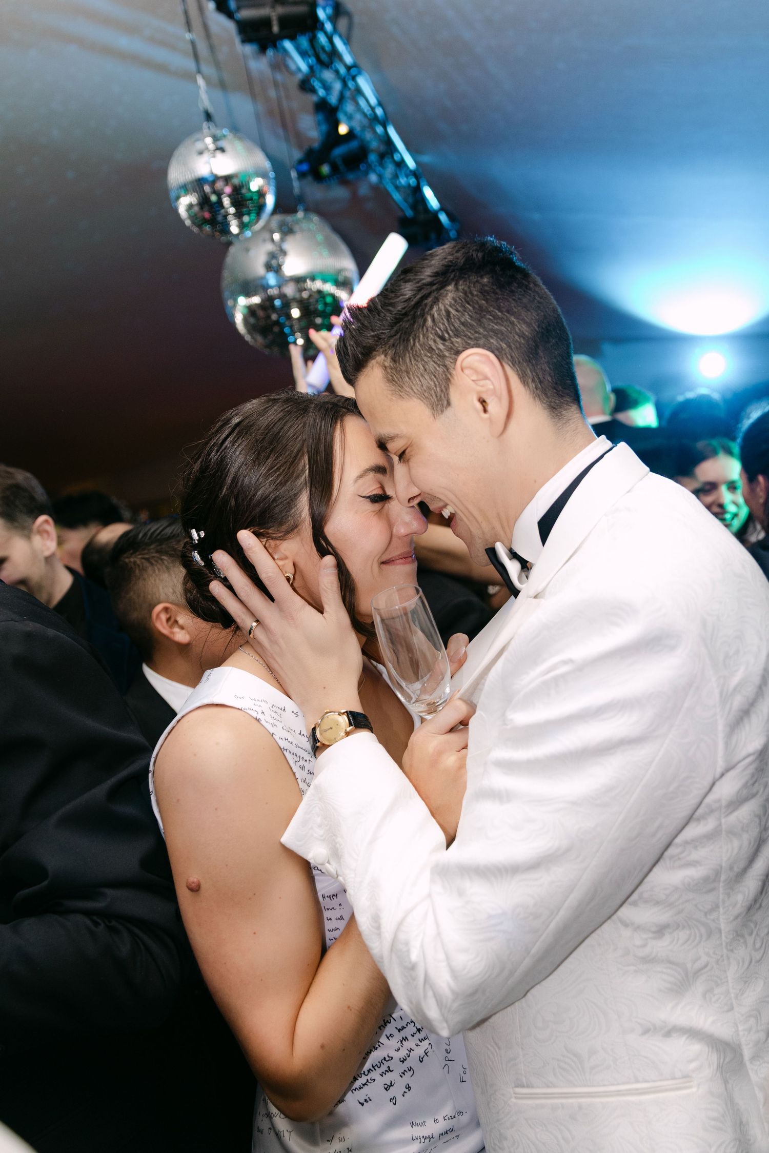 Bride and groom share romantic kiss on dance floor under disco balls at wedding reception.