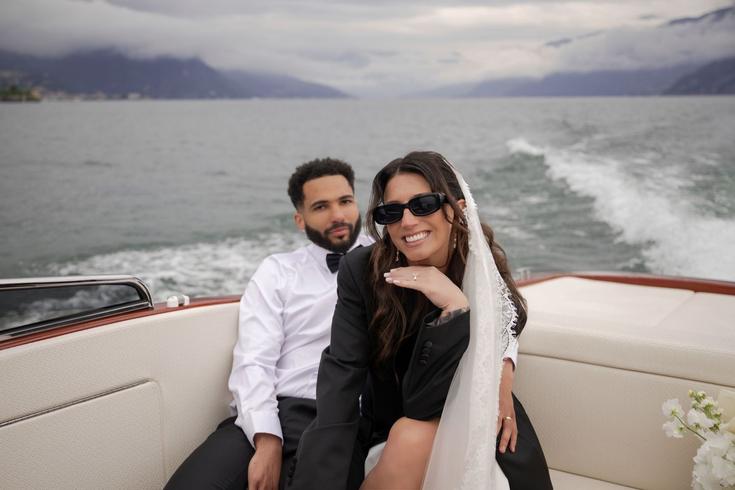 Happy couple sitting on a luxury boat with scenic lake and mountain views behind them.