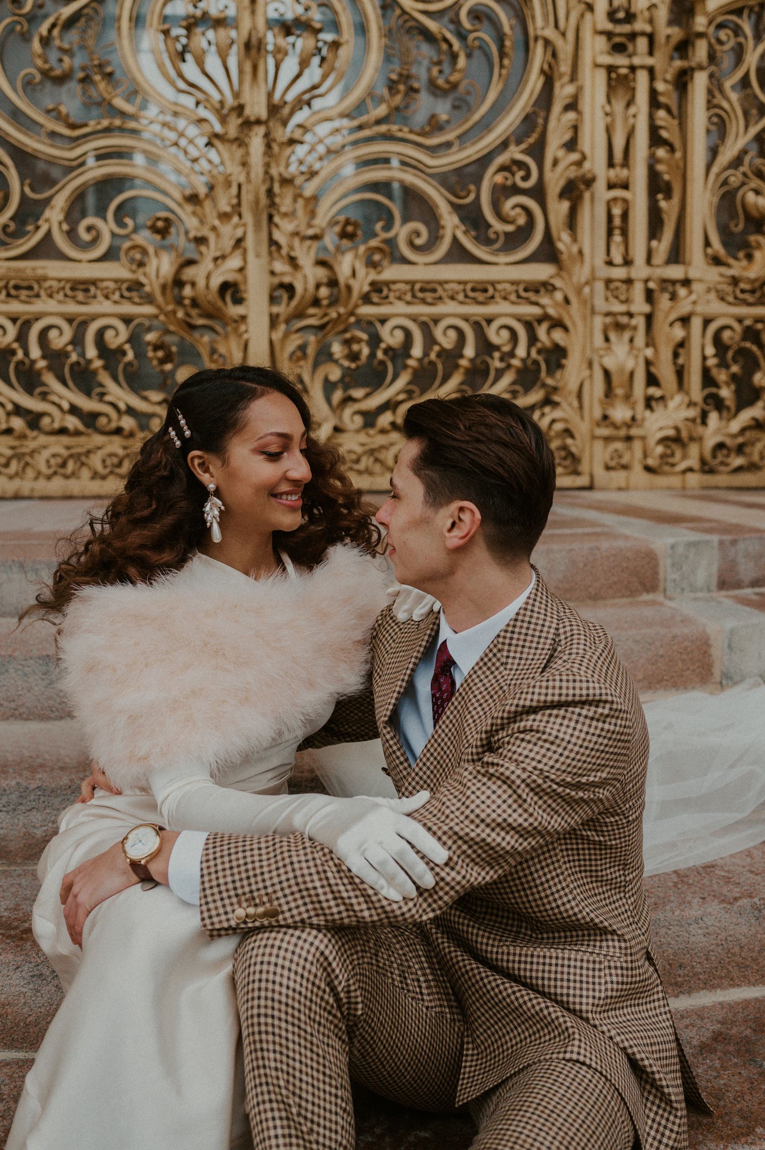 Intimate wedding portrait of couple sitting on stone steps with ornate gold background.