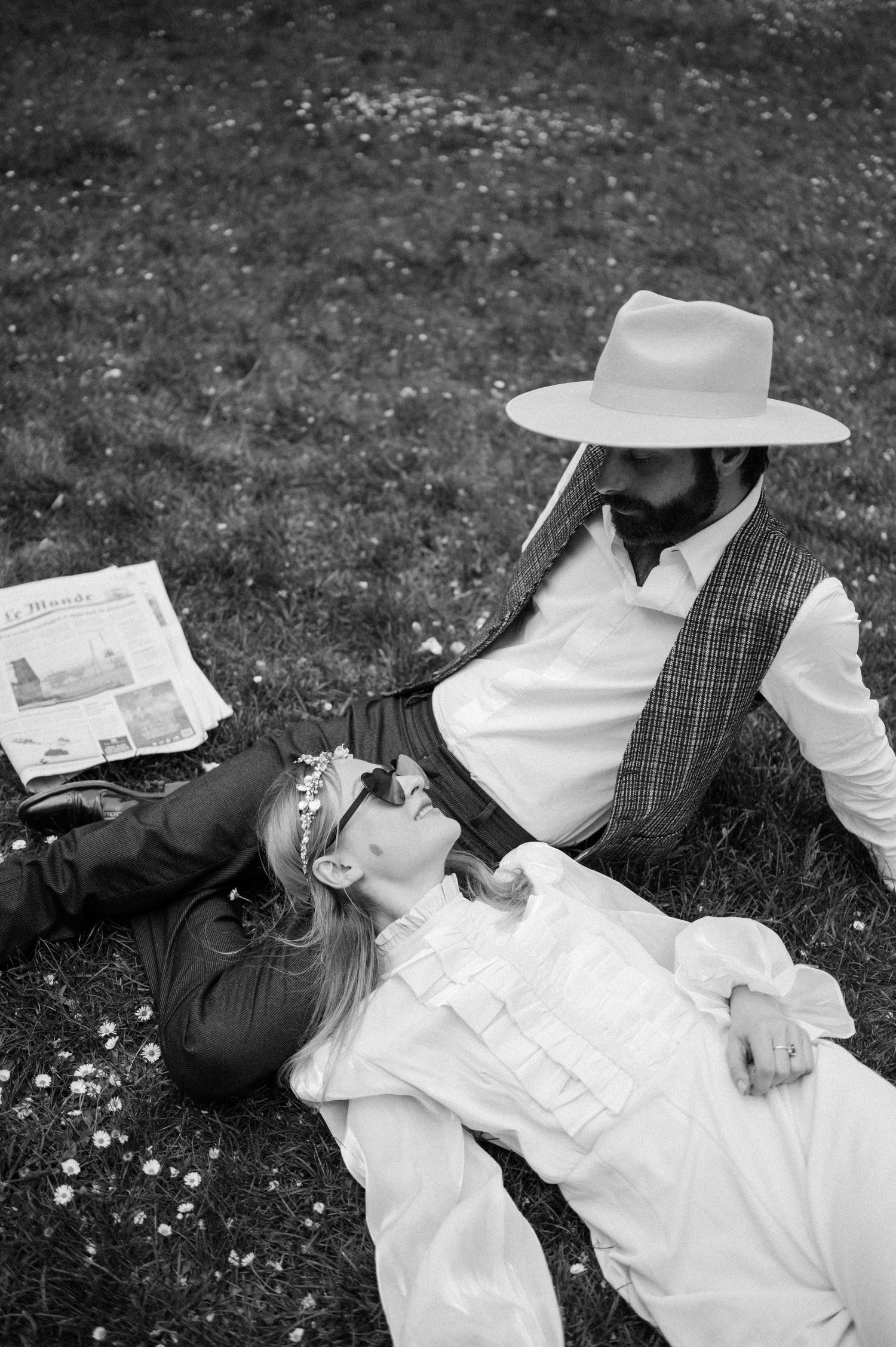 Black and white portrait of couple relaxing on grass with newspaper and vintage styling.