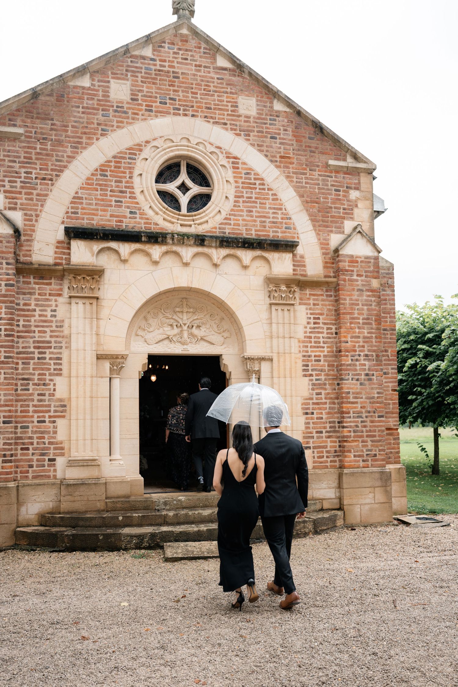 Couple sharing an umbrella in front of a historic brick archway on a rainy day.